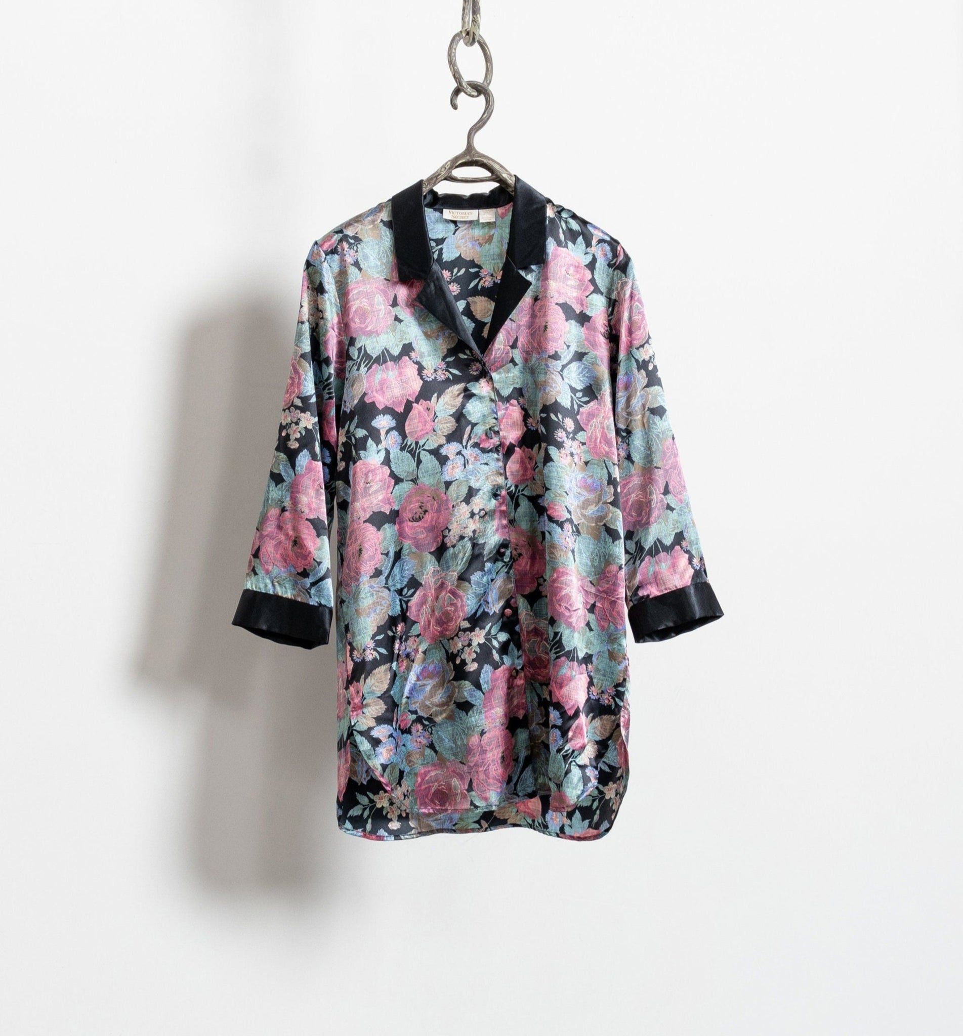 A vintage satin finish floral mini dress with a black collar, pink roses, and a glossy finish, displayed on a hanger against a white background.