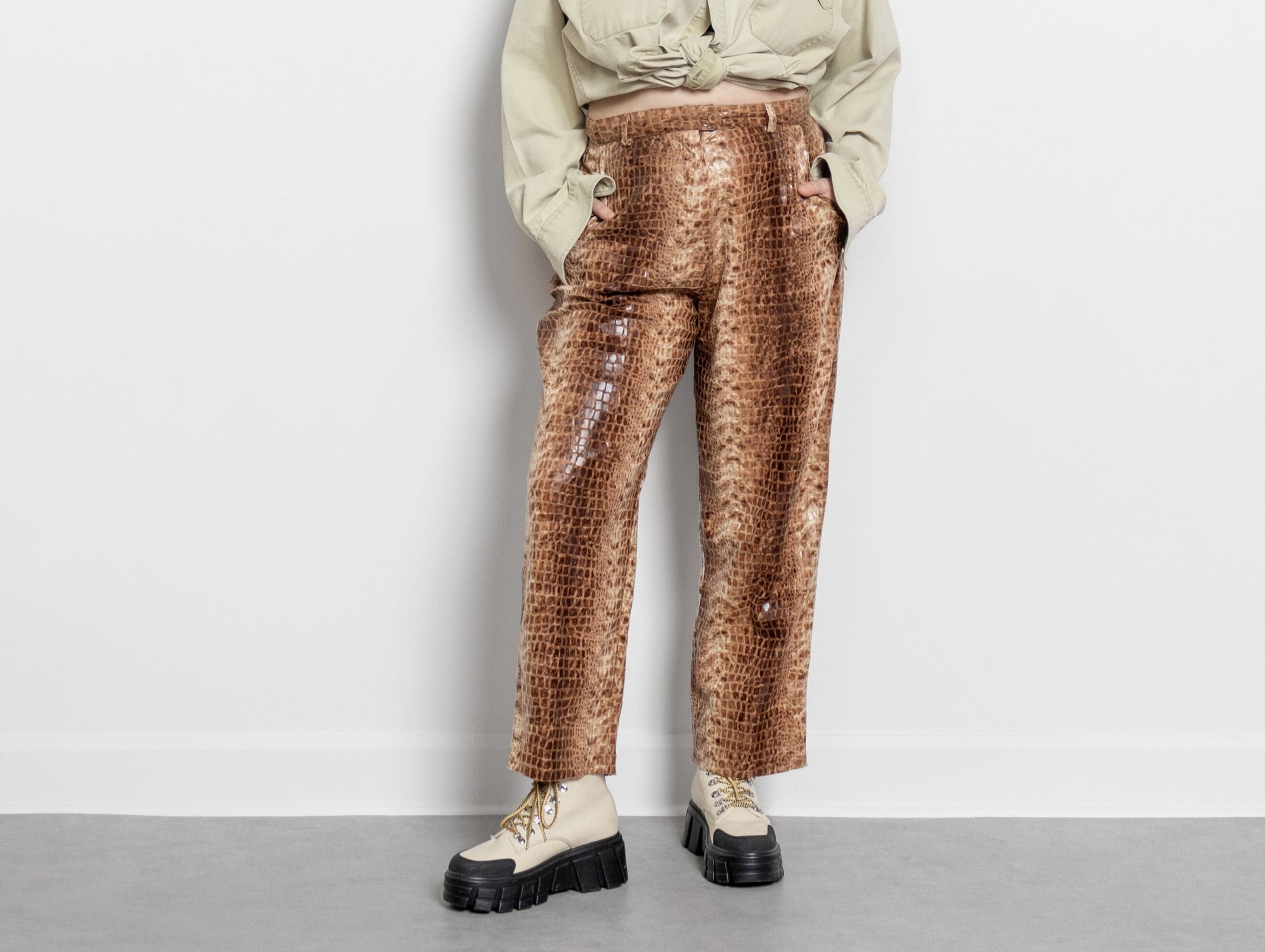A person wearing high waist faux leather trousers with an alligator skin pattern, paired with a beige jacket and white shoes.