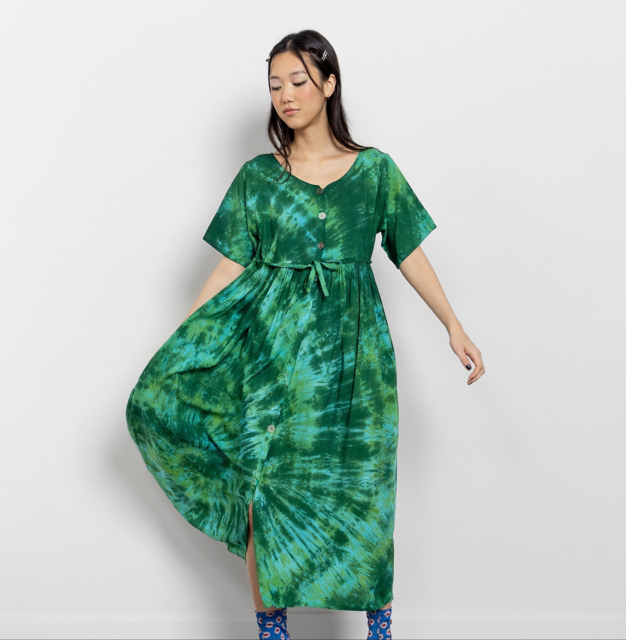 A woman modeling a vintage 90's flowy tie-dye short-sleeve maxi dress in bright green tie-dye design with waist tie and front button detail.