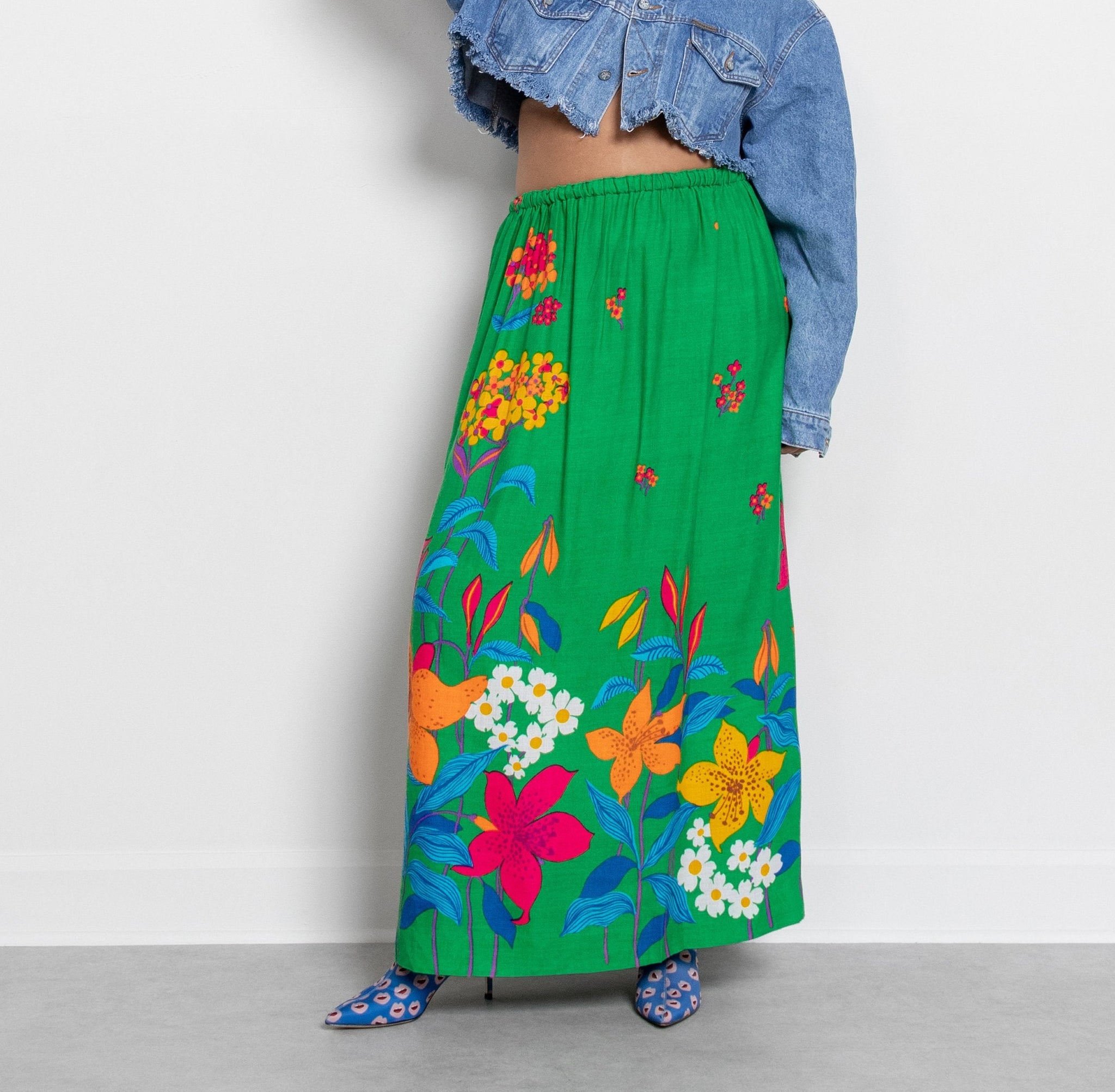 A person wearing a vibrant green floral print maxi skirt with an elastic waistband, paired with a blue-patterned top and blue shoes.
