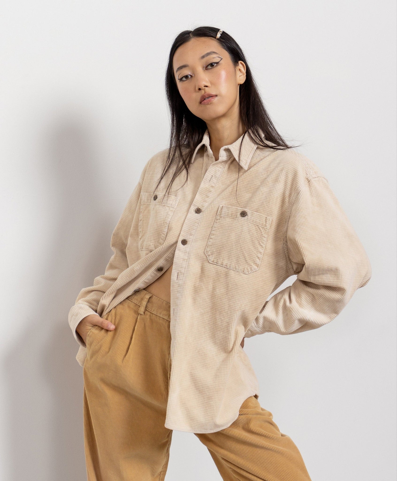Woman wearing a beige shirt and brown pants against a white background