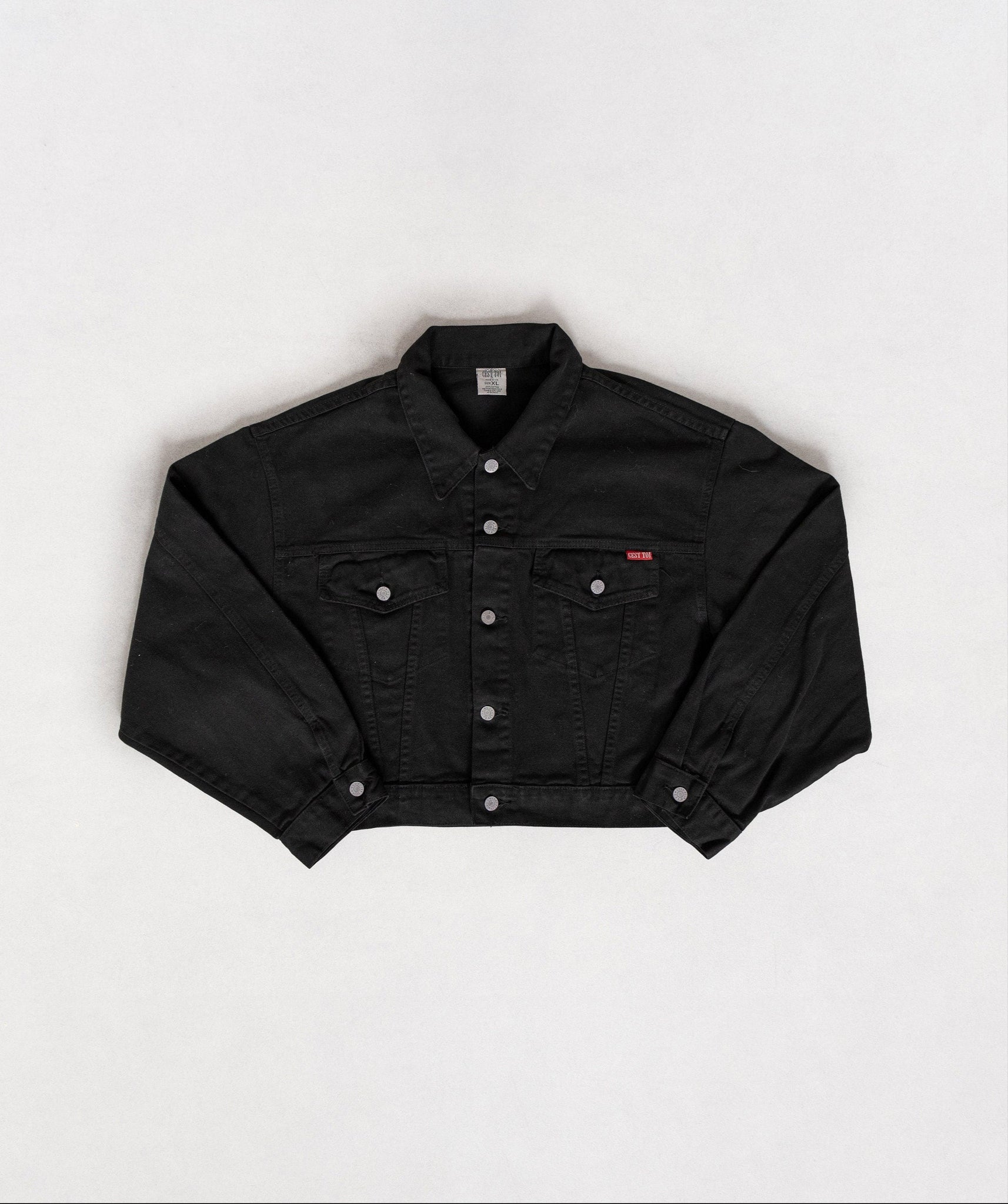 A cropped black denim jacket with breast pockets and a front zipper, displayed on a plain background.