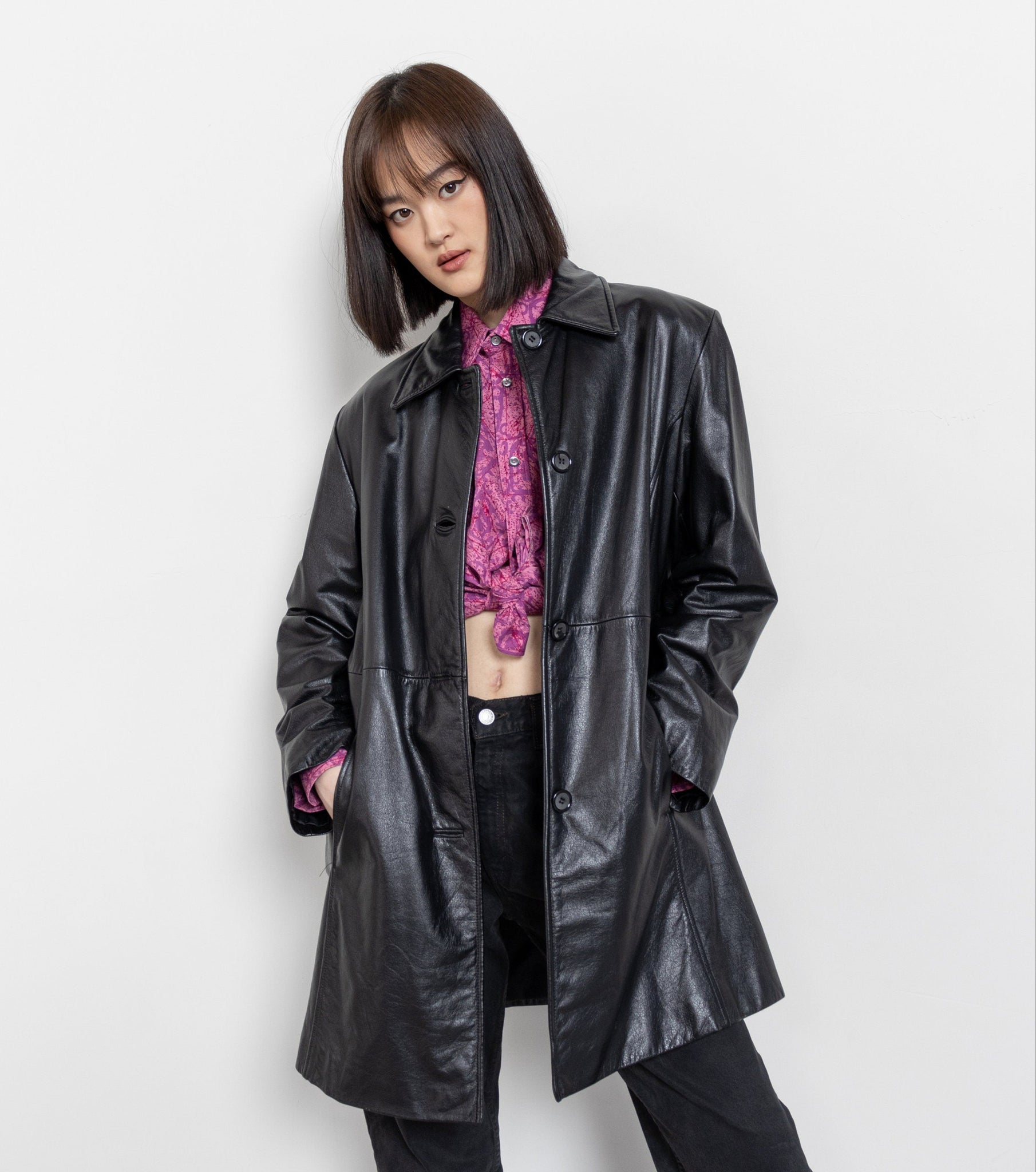 Person wearing a black leather coat over a pink top on a white background