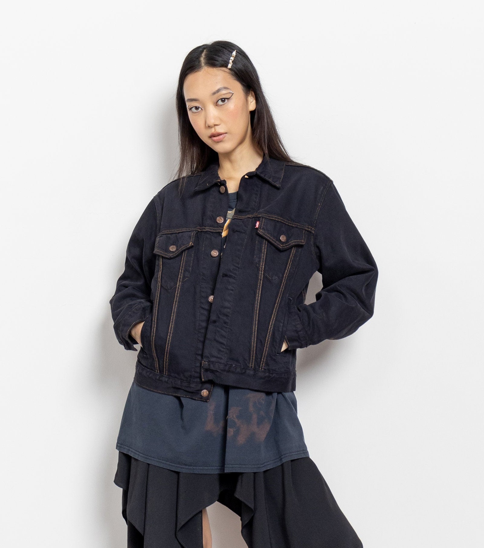 A woman wearing a vintage black denim jacket with a collared shirt underneath. The jacket has a button-up front and features pockets.
