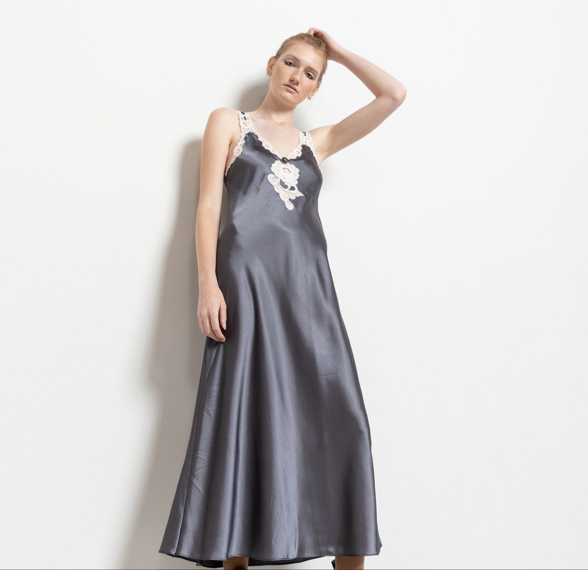 A woman modeling a vintage gray satin slip dress with lace trim and a plunging neckline.