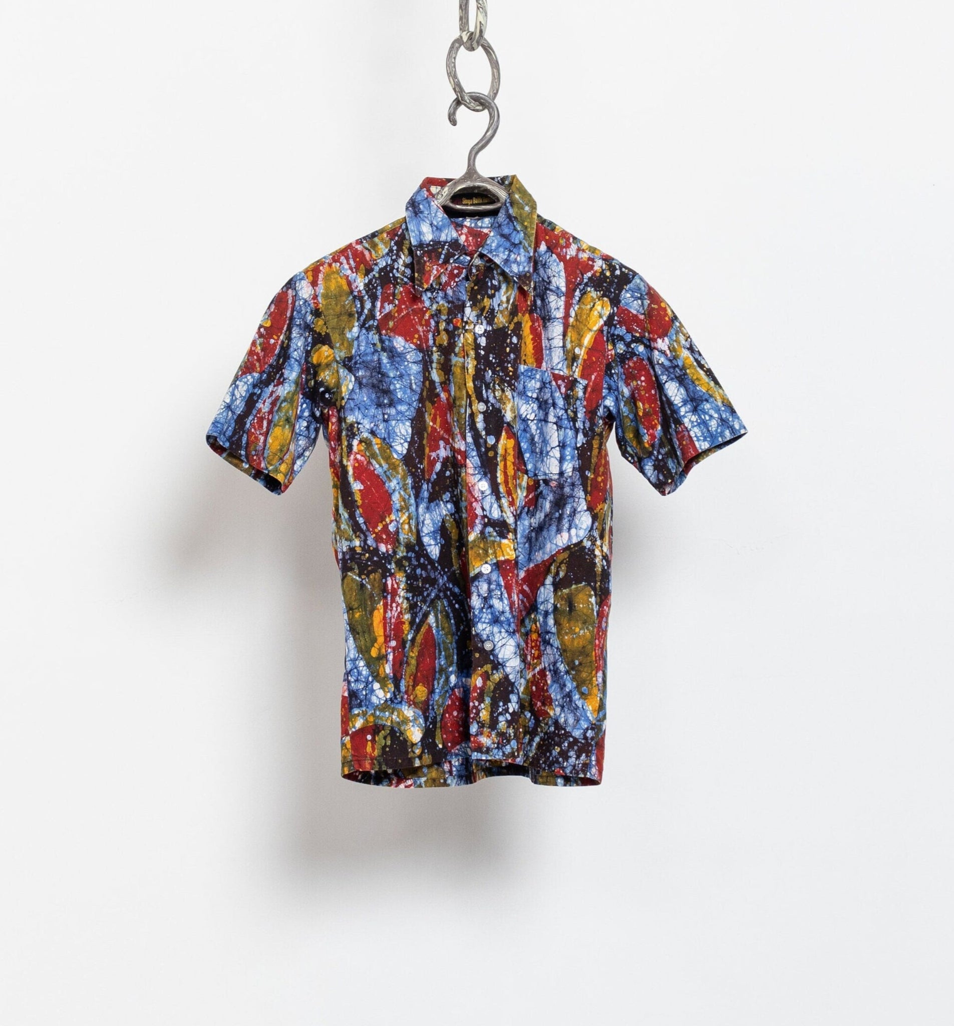 A vintage cotton batik dyed shirt with a multicolored geometric pattern, displayed on a hanger against a white wall.