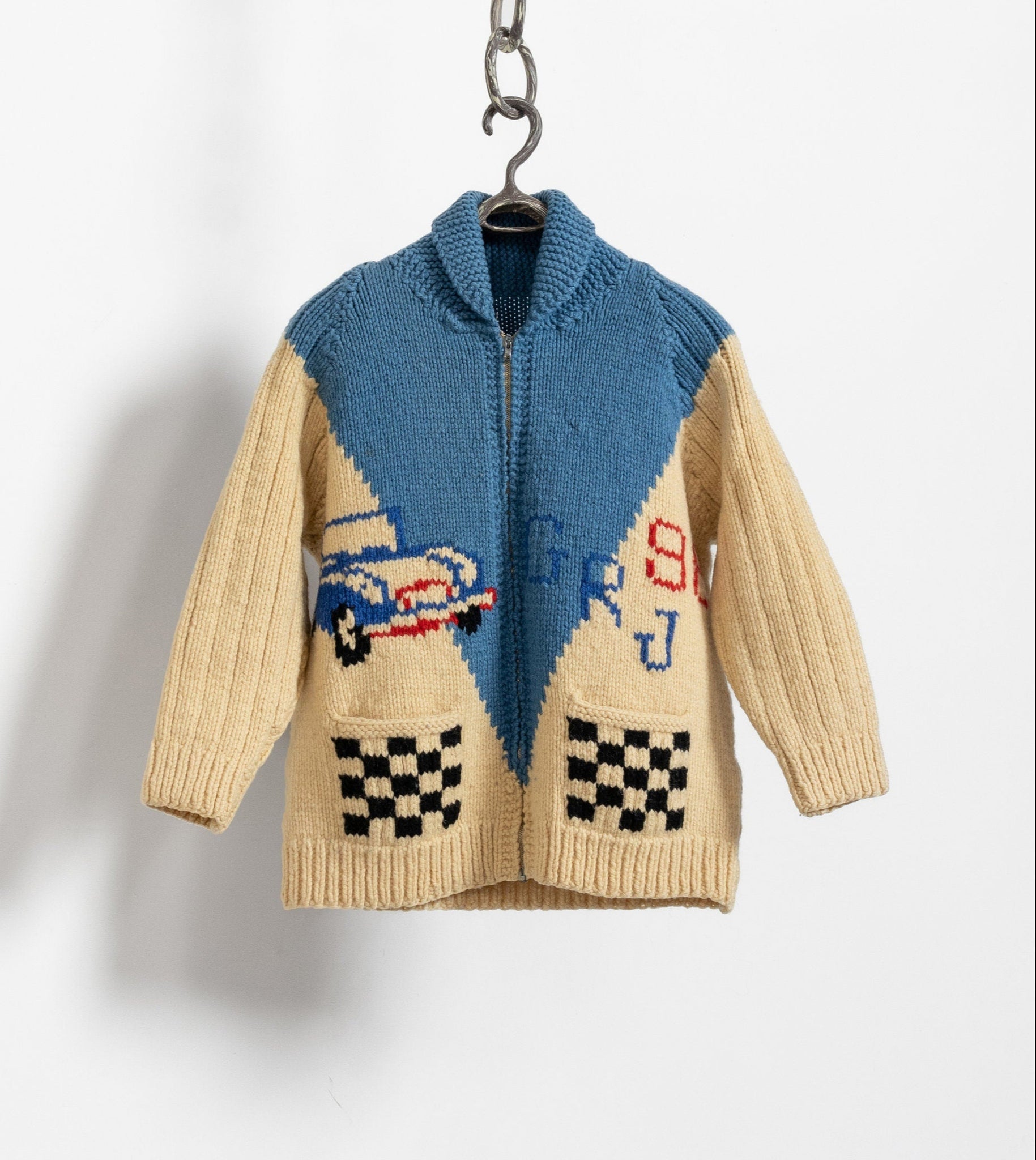 A vintage 90's hand knit multicolor cardigan hanging on a hanger, featuring a grandpa style with two front pockets and a car graphic detail.