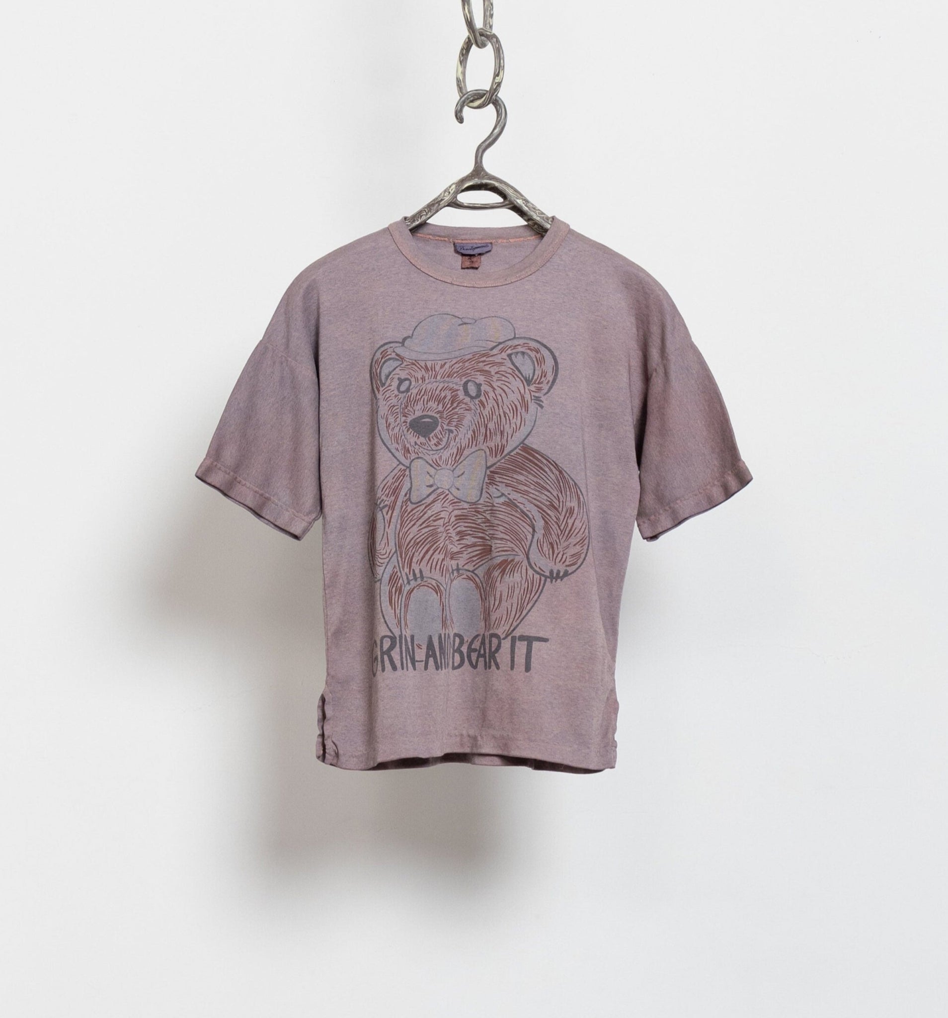 A vintage brown oversized t-shirt with a crew neck and short sleeves, featuring a graphic of a teddy bear wearing a bow tie and the phrase 'grin and bear it' on the front.