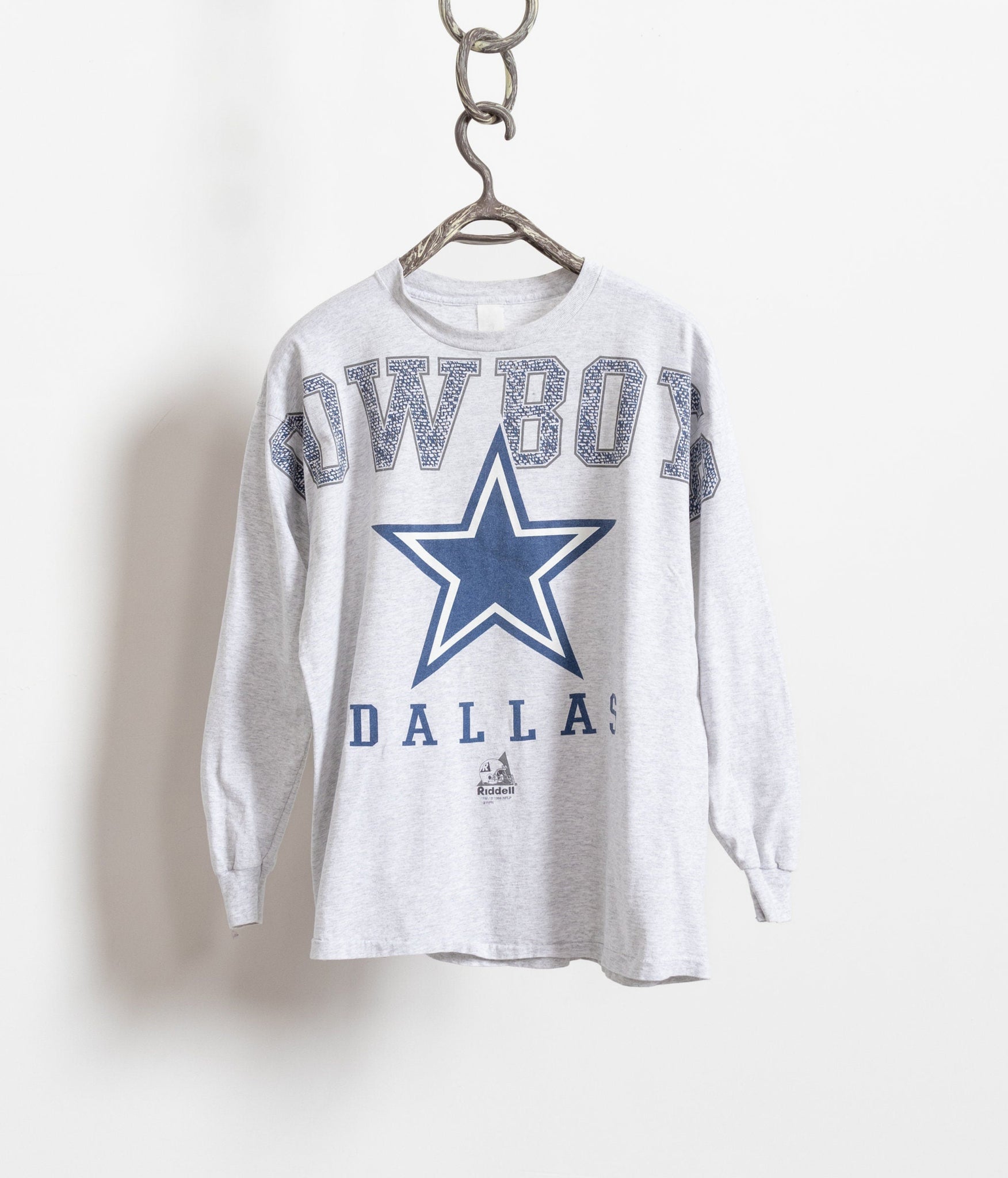 Vintage 90's heather grey Dallas Cowboys long sleeve crew neck t-shirt displayed on a hanger, featuring a navy blue graphic with the Dallas Cowboys star and text.