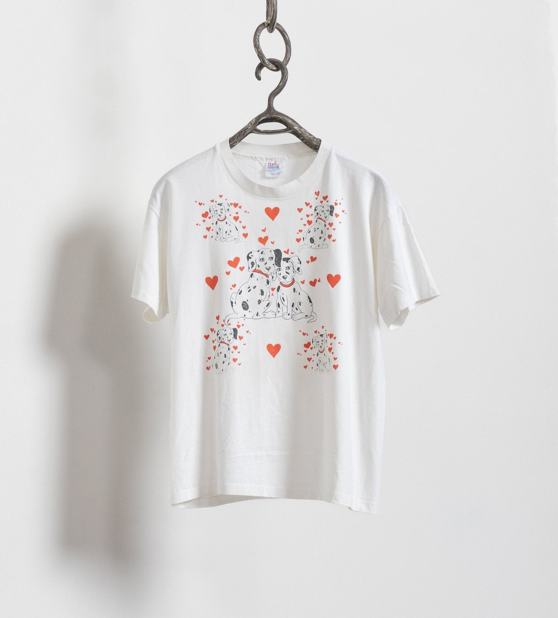 A white poly-cotton t-shirt with a graphic print of two Dalmatian dogs and red cartoon hearts, displayed on a hanger against a white background.
