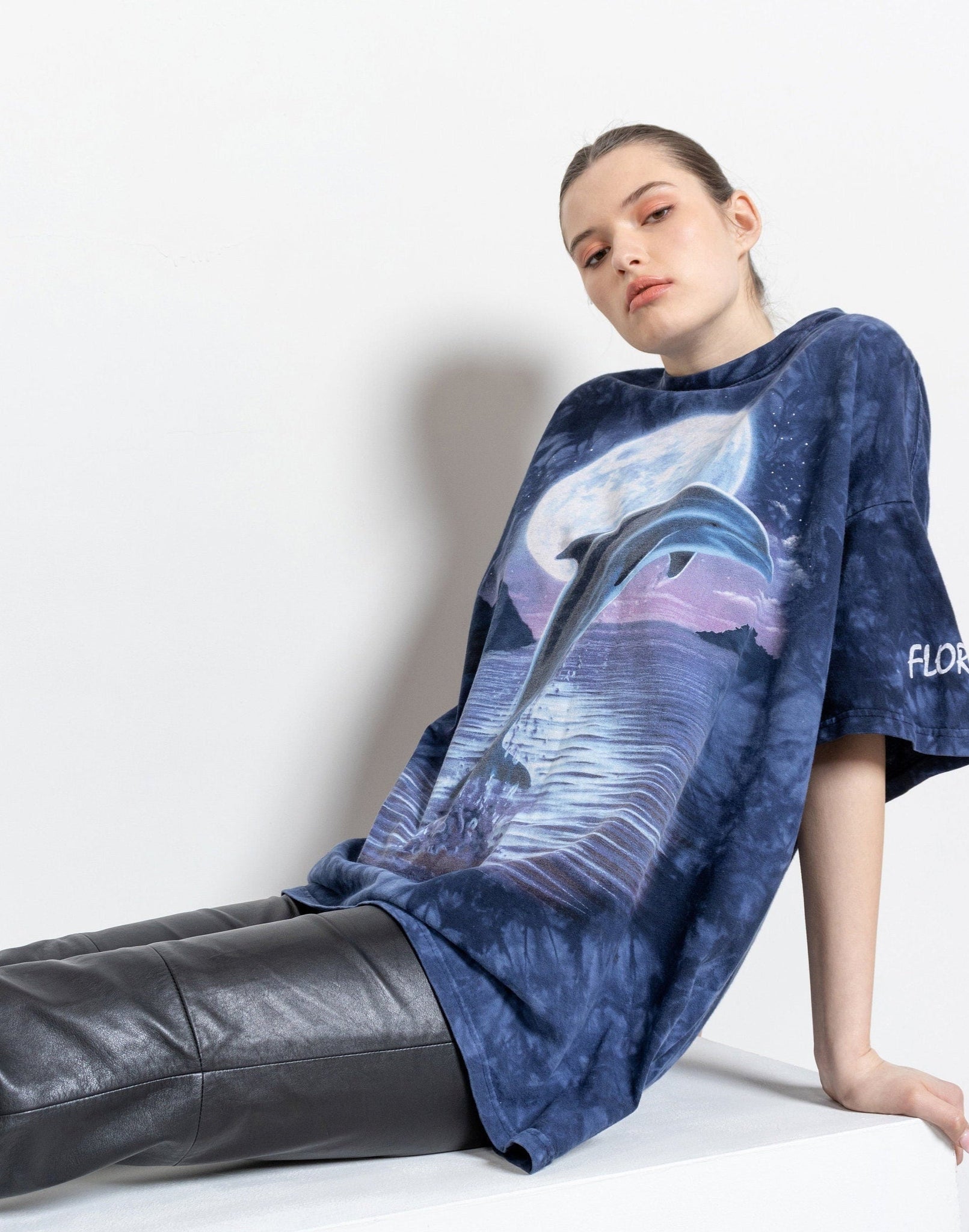 A person sitting against a white background wearing a navy blue tie-dye t-shirt with a dolphin graphic.