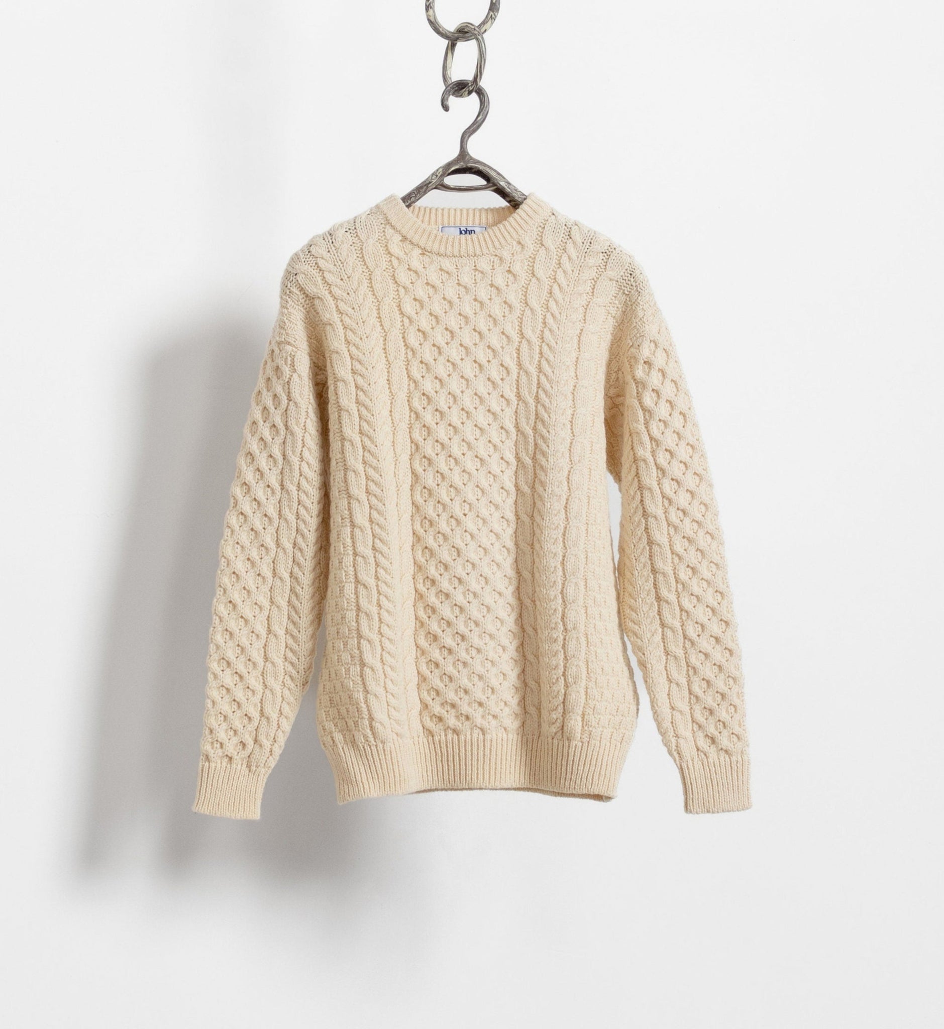 A vintage creamy beige cable knit wool Irish pullover sweater hanging against a white background.