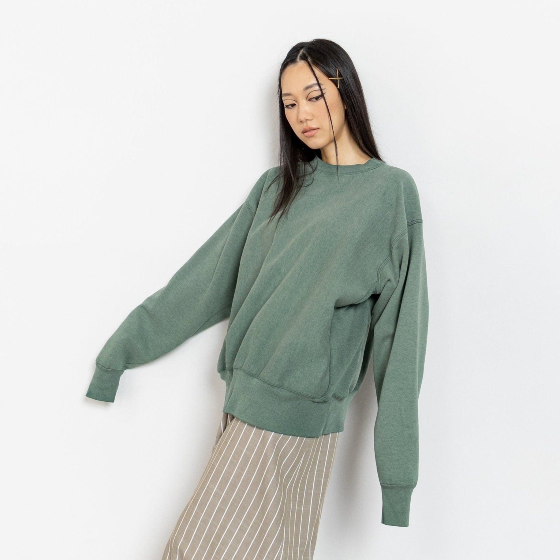 A woman wearing a green poly-cotton-blend pullover sweatshirt with a round neckline and long sleeves.