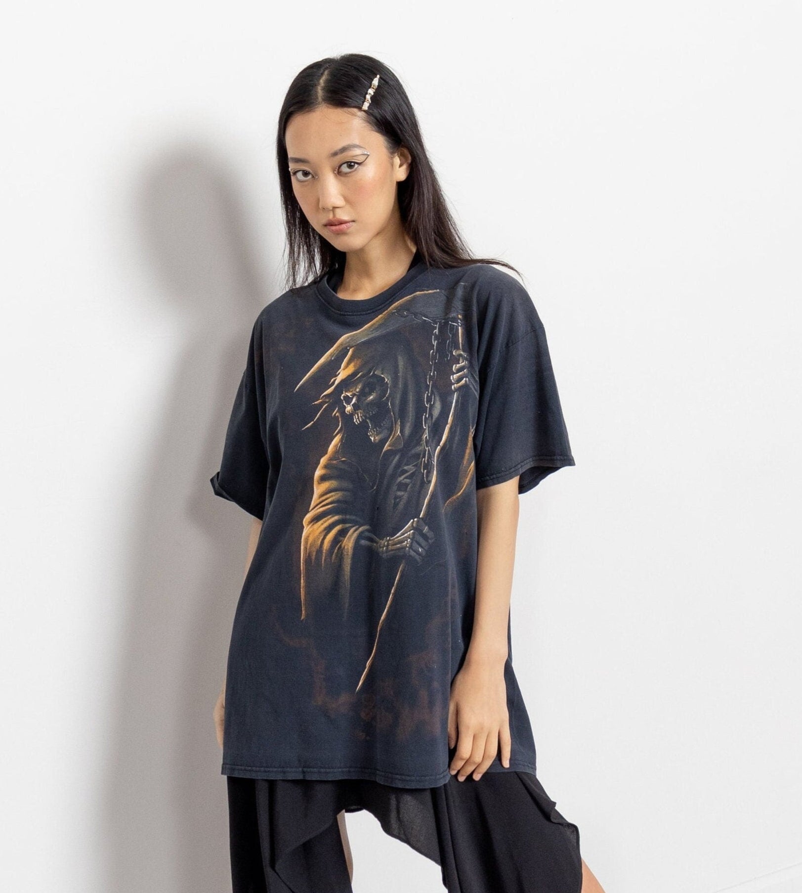 A person wearing a vintage oversize black t-shirt with a graphic of a angel of death, standing against a white background.