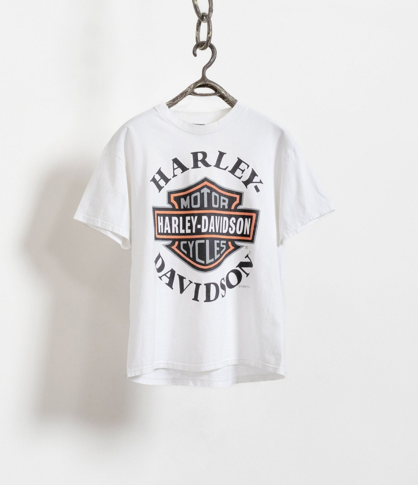 Harley Davidson graphic t-shirt in white with orange and black logo on the front, displayed on a hanger against a white background.