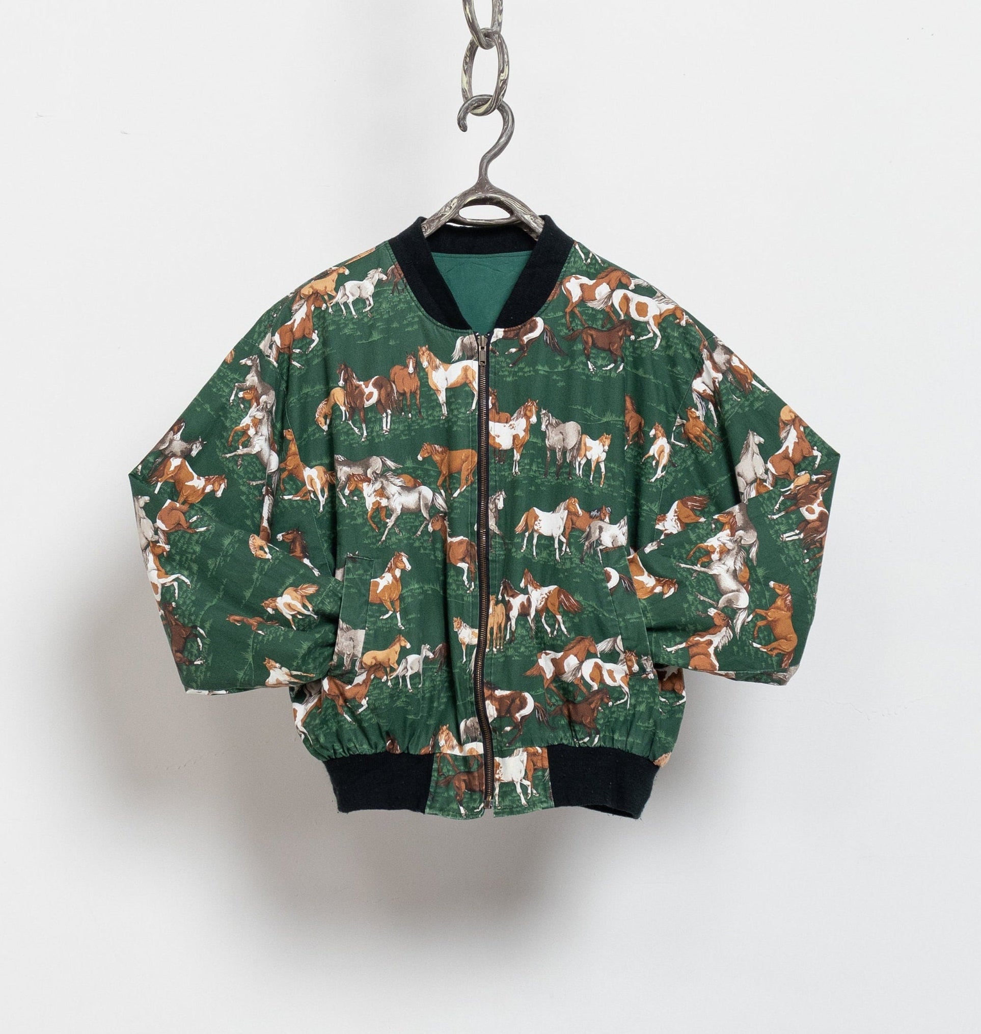 Green bomber jacket with horse pattern on a hanger against a white background