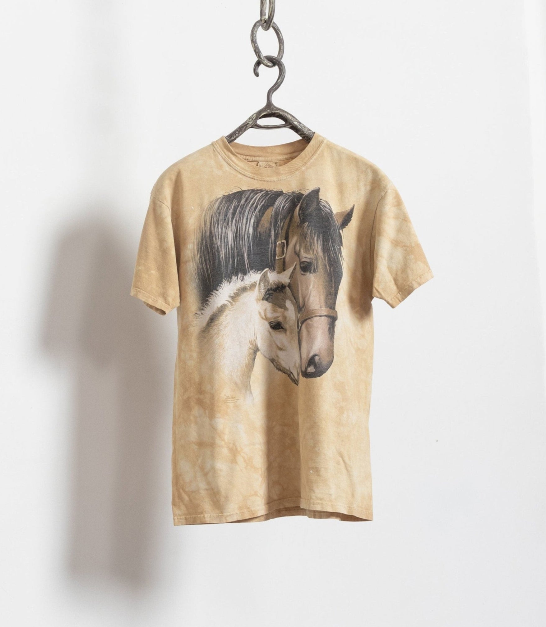 A vintage 90's faded yellow/brown distressed horse family graphic tee hanging on a hanger against a white background.