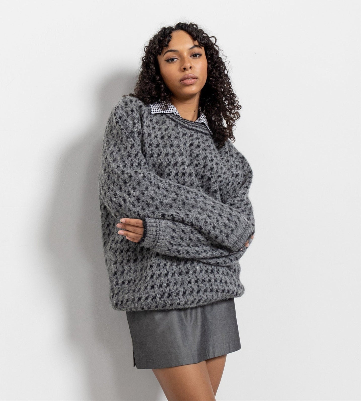Woman wearing a gray patterned sweater and skirt against a white background