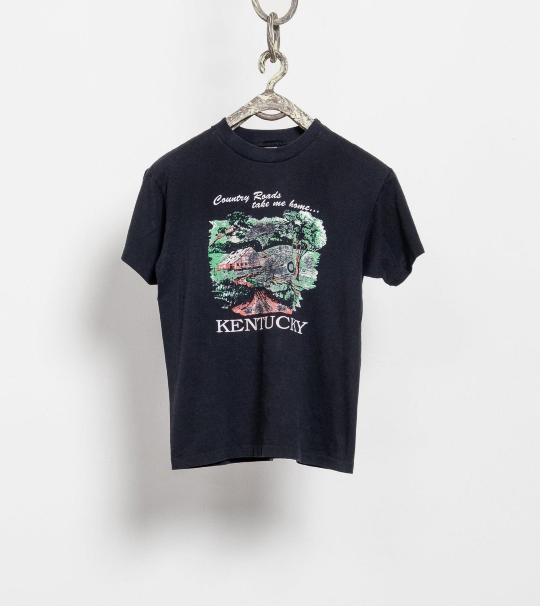 Vintage 90's black short sleeve graphic tee with 'Kentucky' text and a green and rustic design, displayed on a hanger.