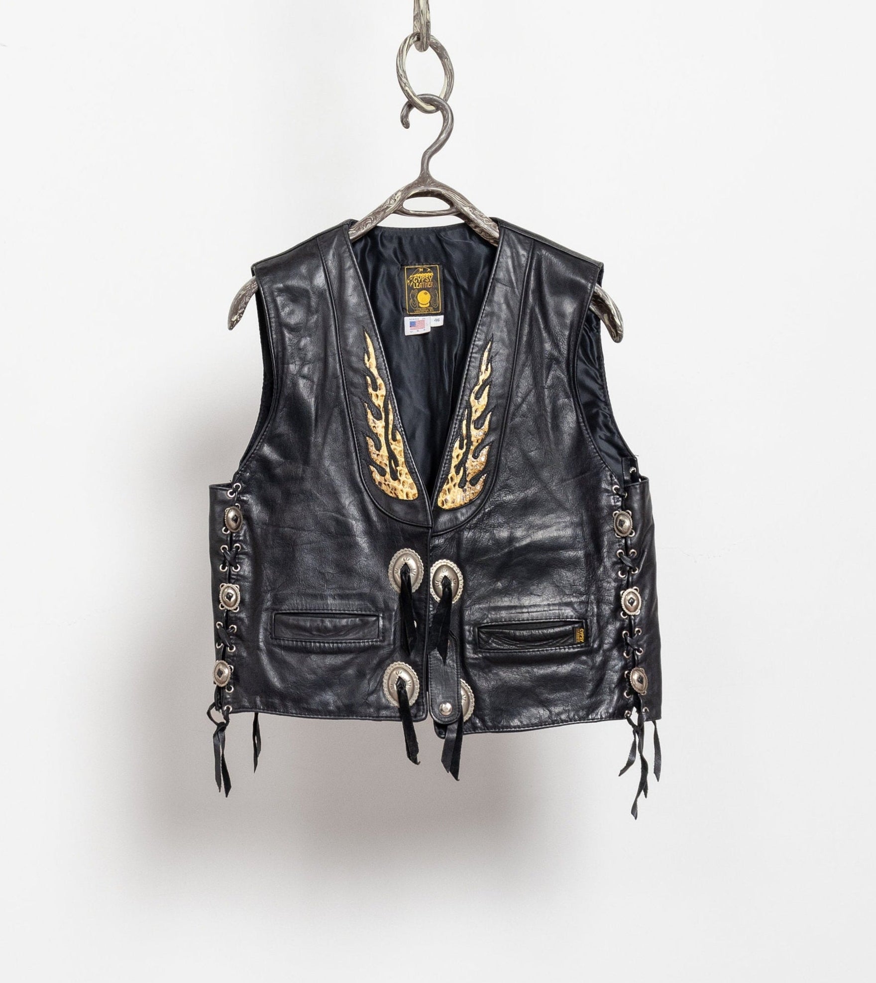 Black leather vest with gold embroidery on a hanger against a white background
