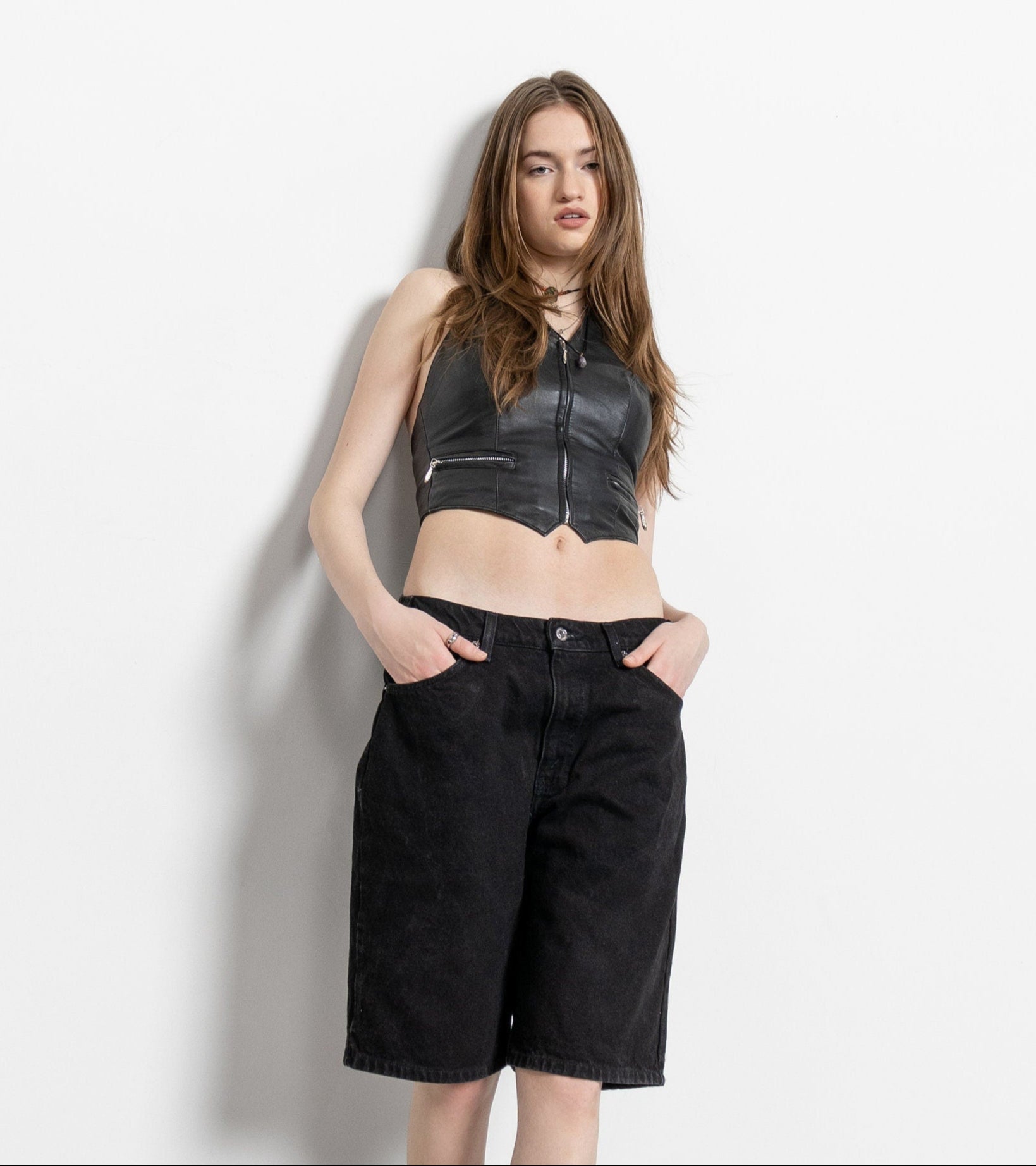 A person wearing high-waisted black denim shorts and a black sleeveless top with a zipper.