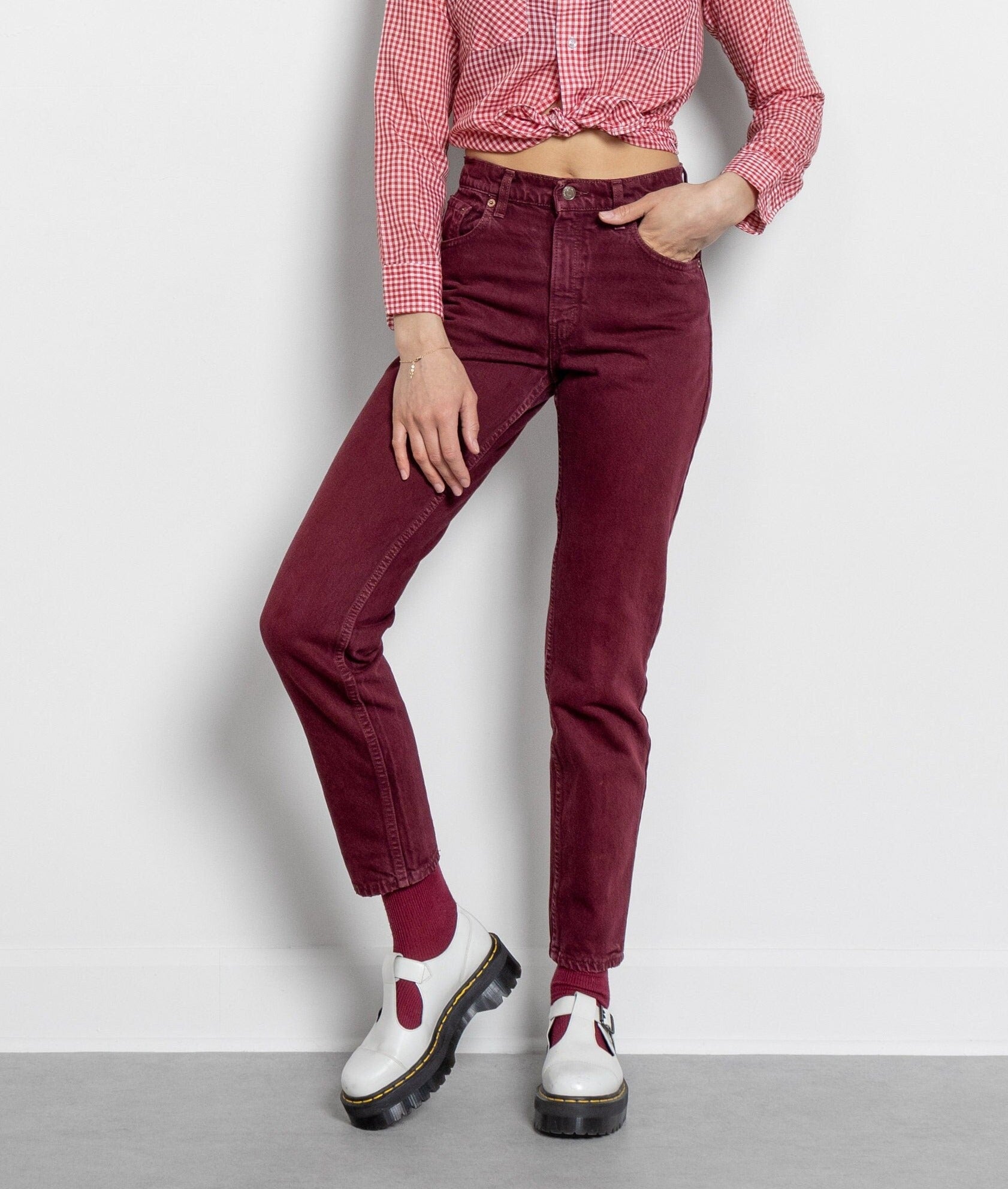 A person standing wearing high waist Levi's 550 jeans in a deep maroon color with a white shirt and white shoes.