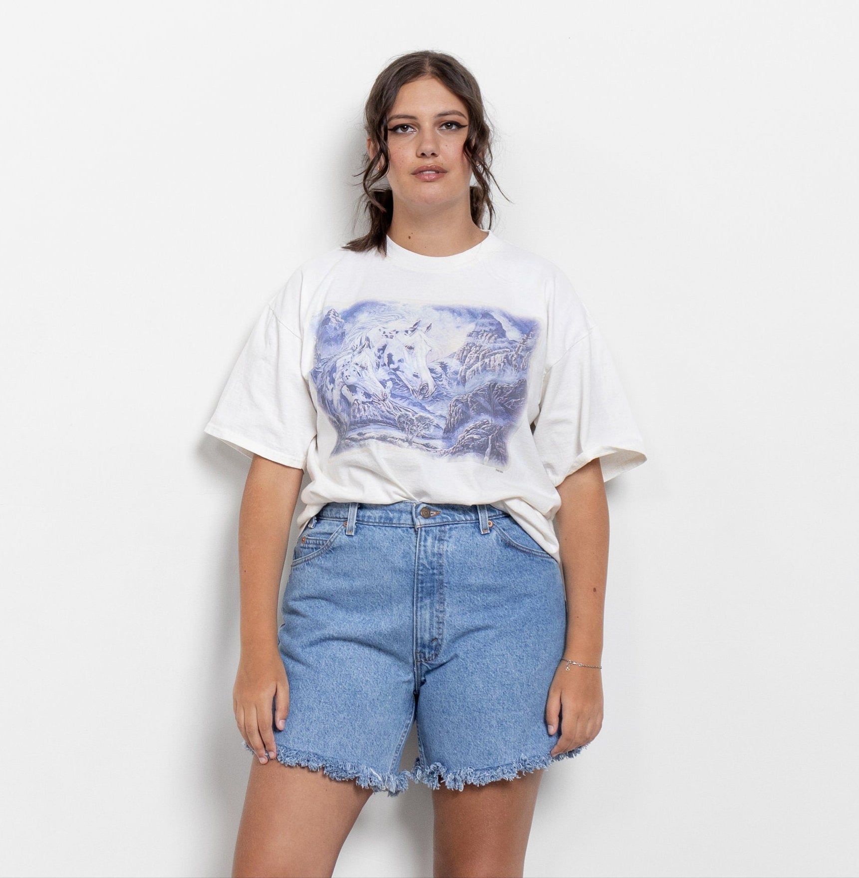 A person wearing a white t-shirt with a blue abstract pattern and high-waisted blue denim shorts with a frayed hem.