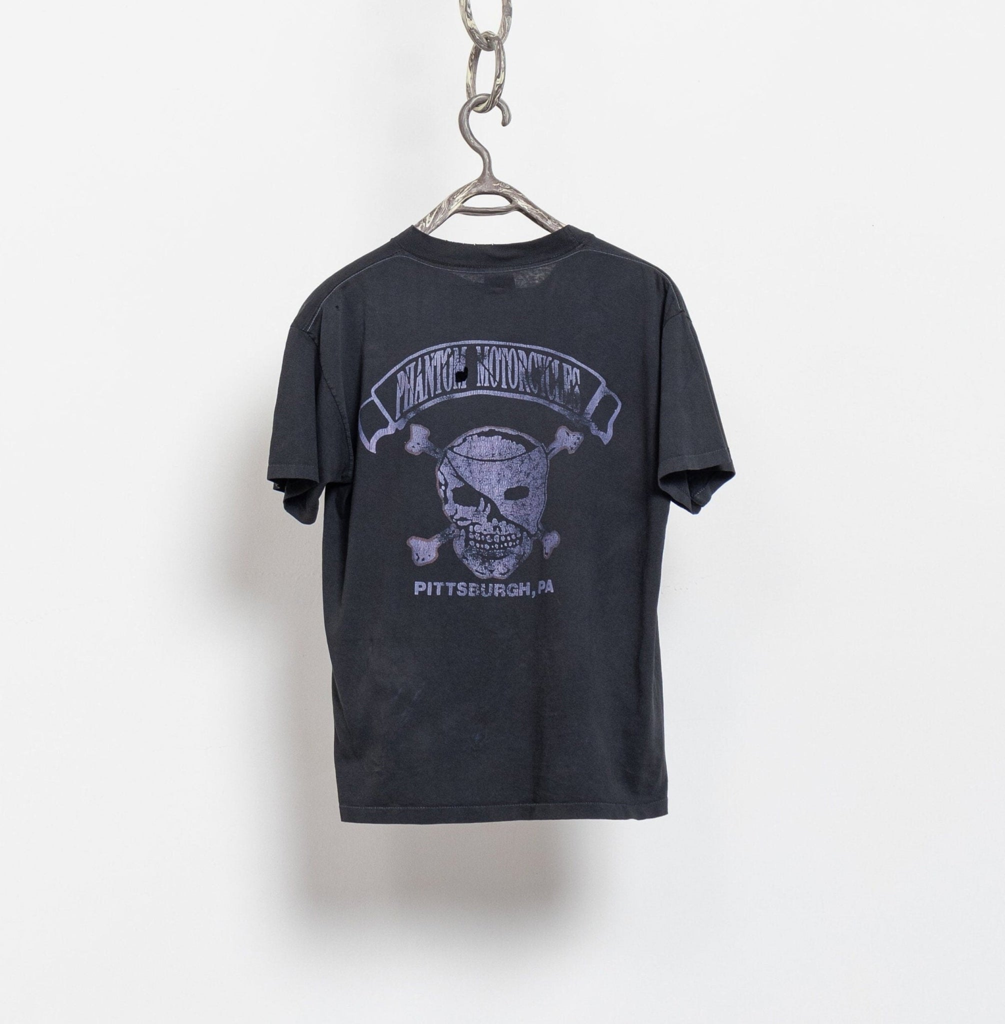 Black t-shirt with a skull and crossbones design on a hanger against a white background