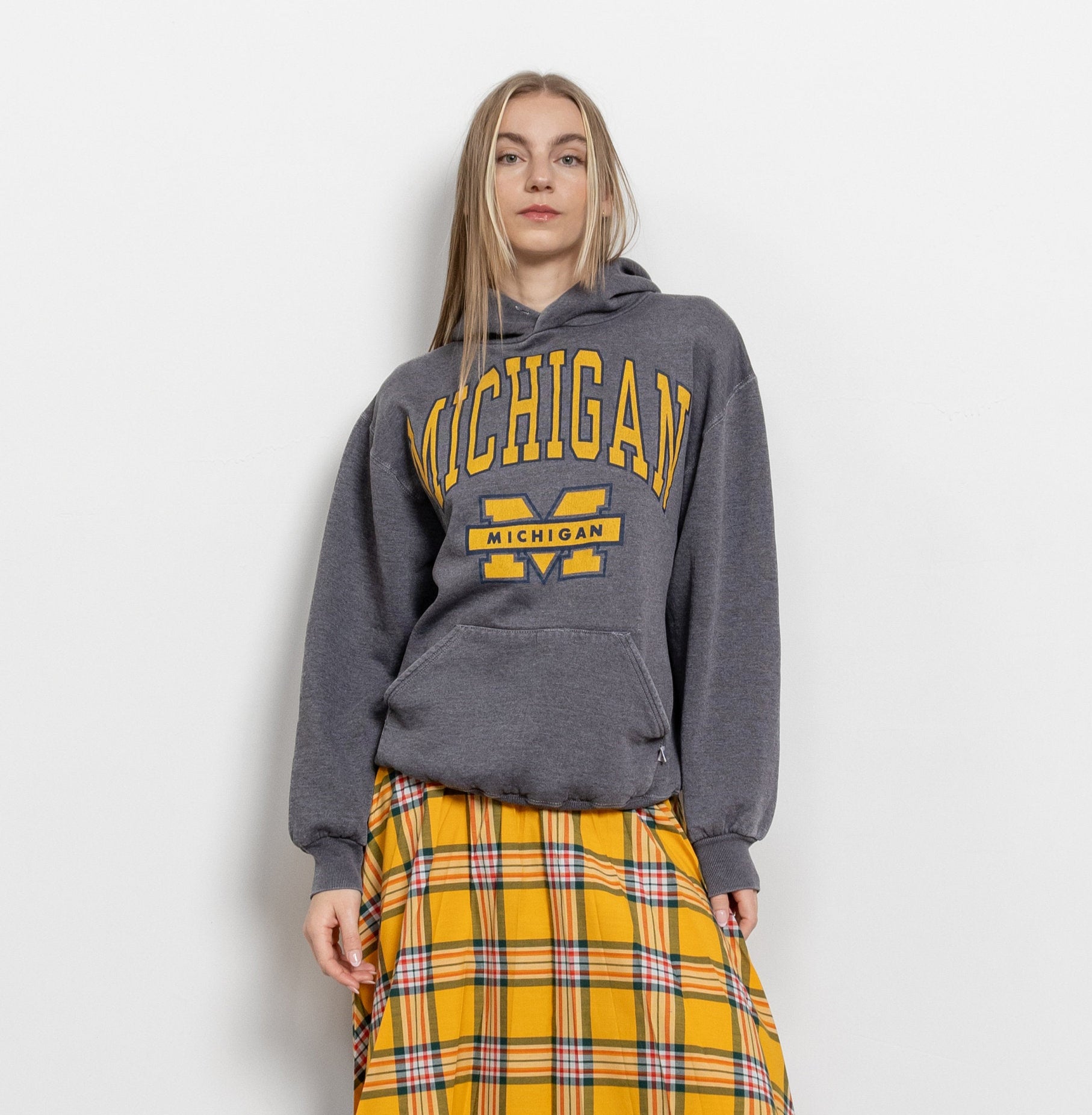 A person wearing a vintage gray Michigan University sweatshirt with yellow varsity lettering, paired with a yellow plaid skirt.