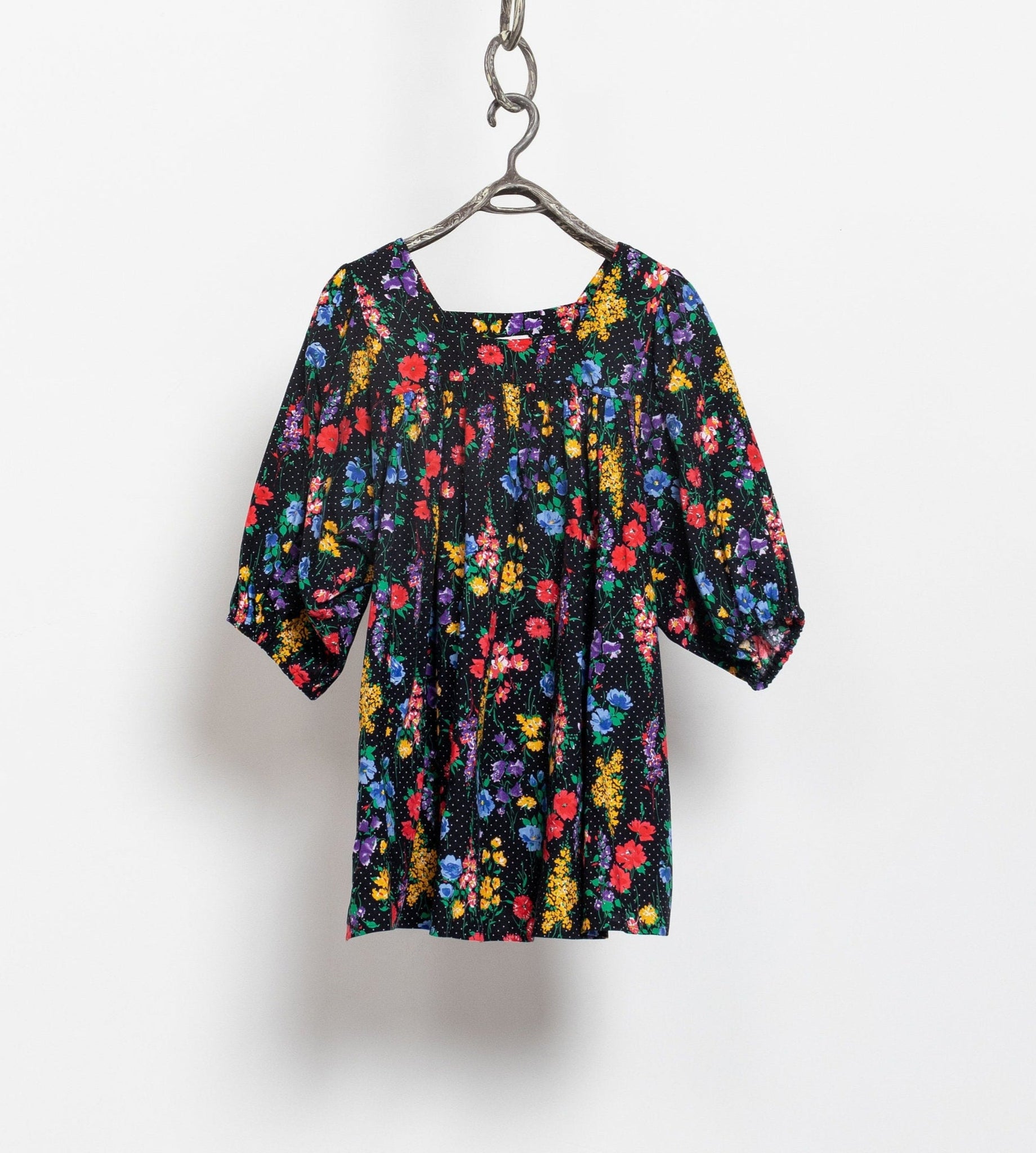 A vintage black floral mini tent dress with puffy half-length sleeves, hanging on a hanger against a white wall.