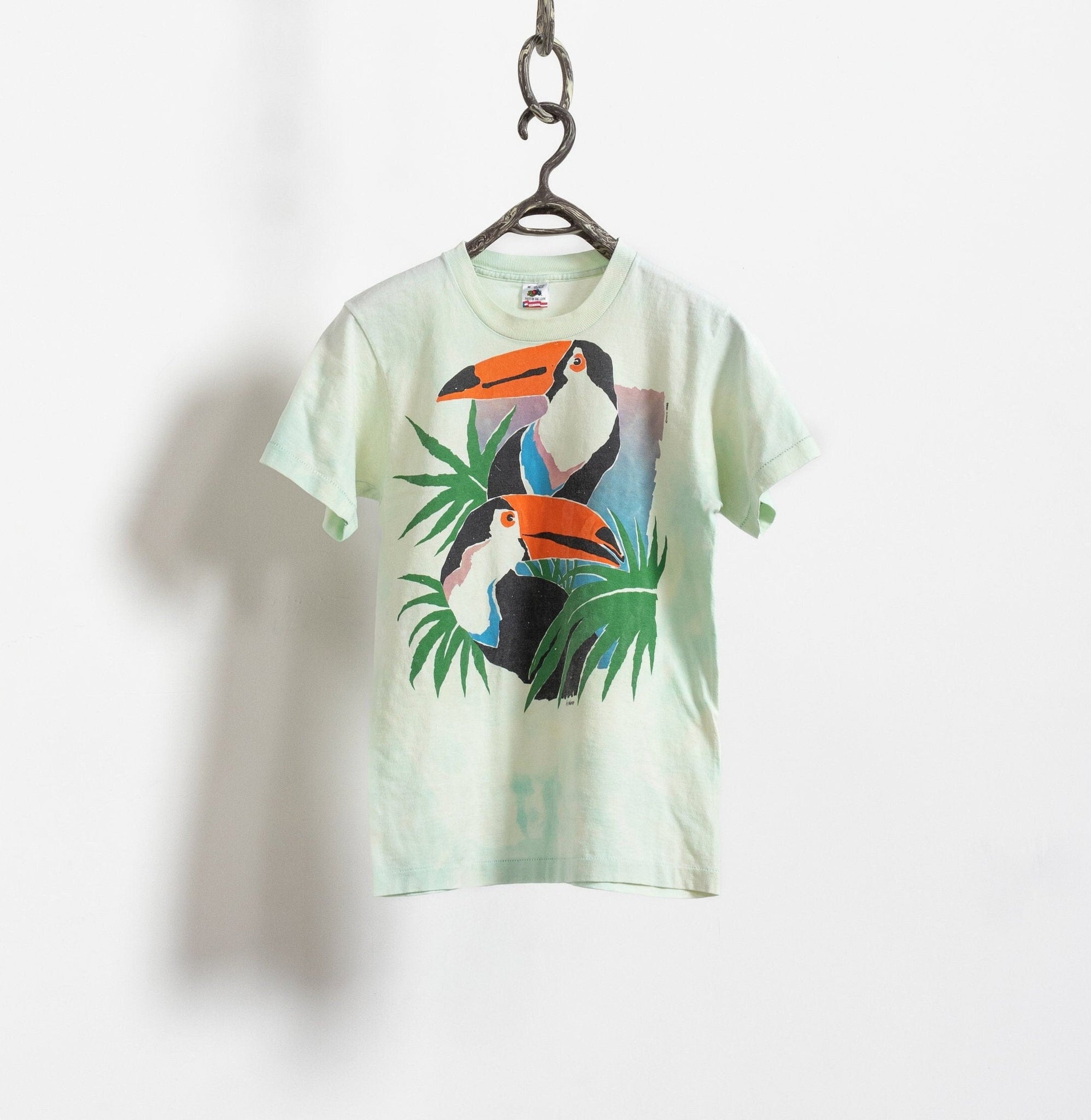 A green tie-dye t-shirt with a vintage parrot print, hanging against a white background.