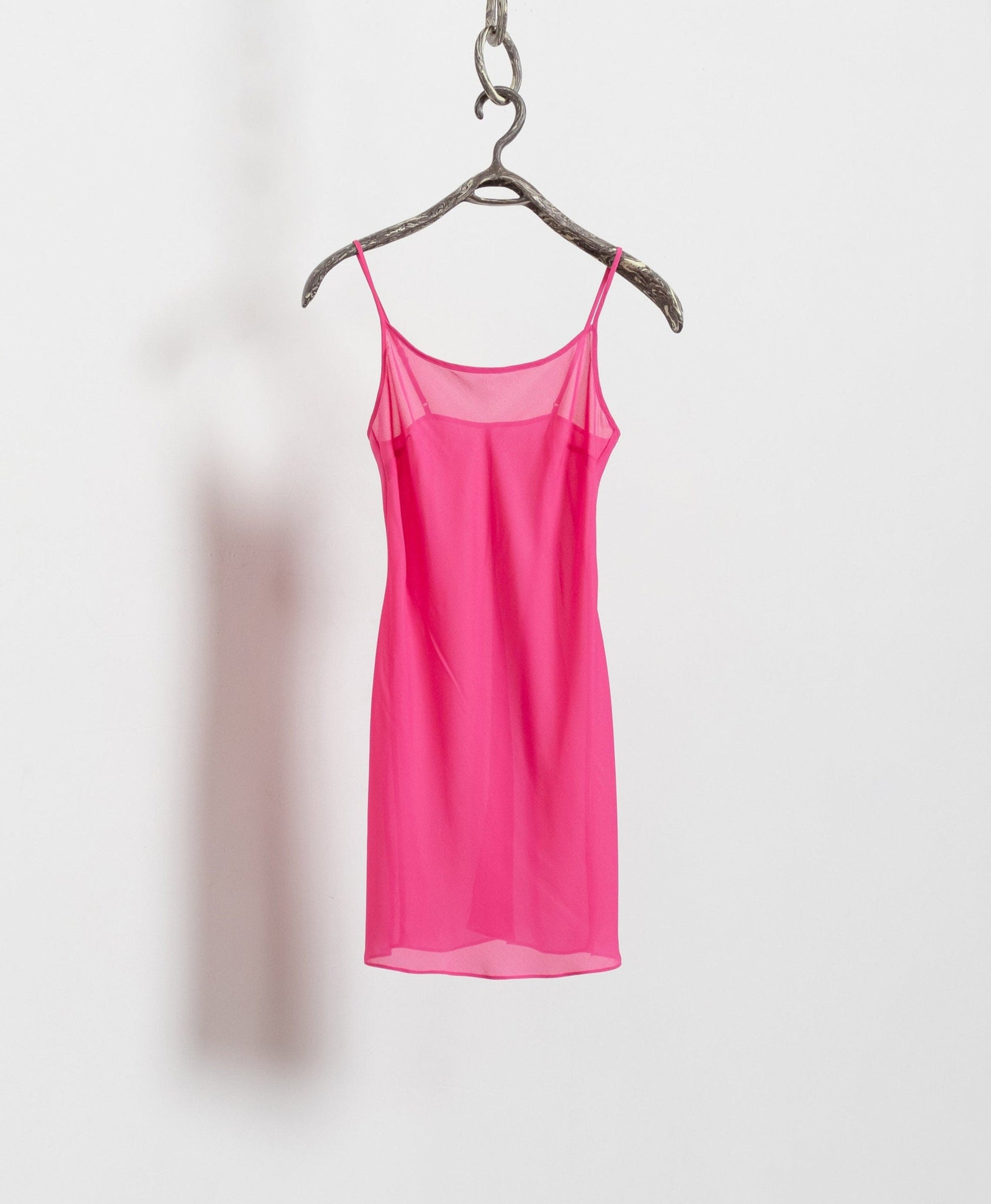Pink slip dress hanging on a hanger against a white background