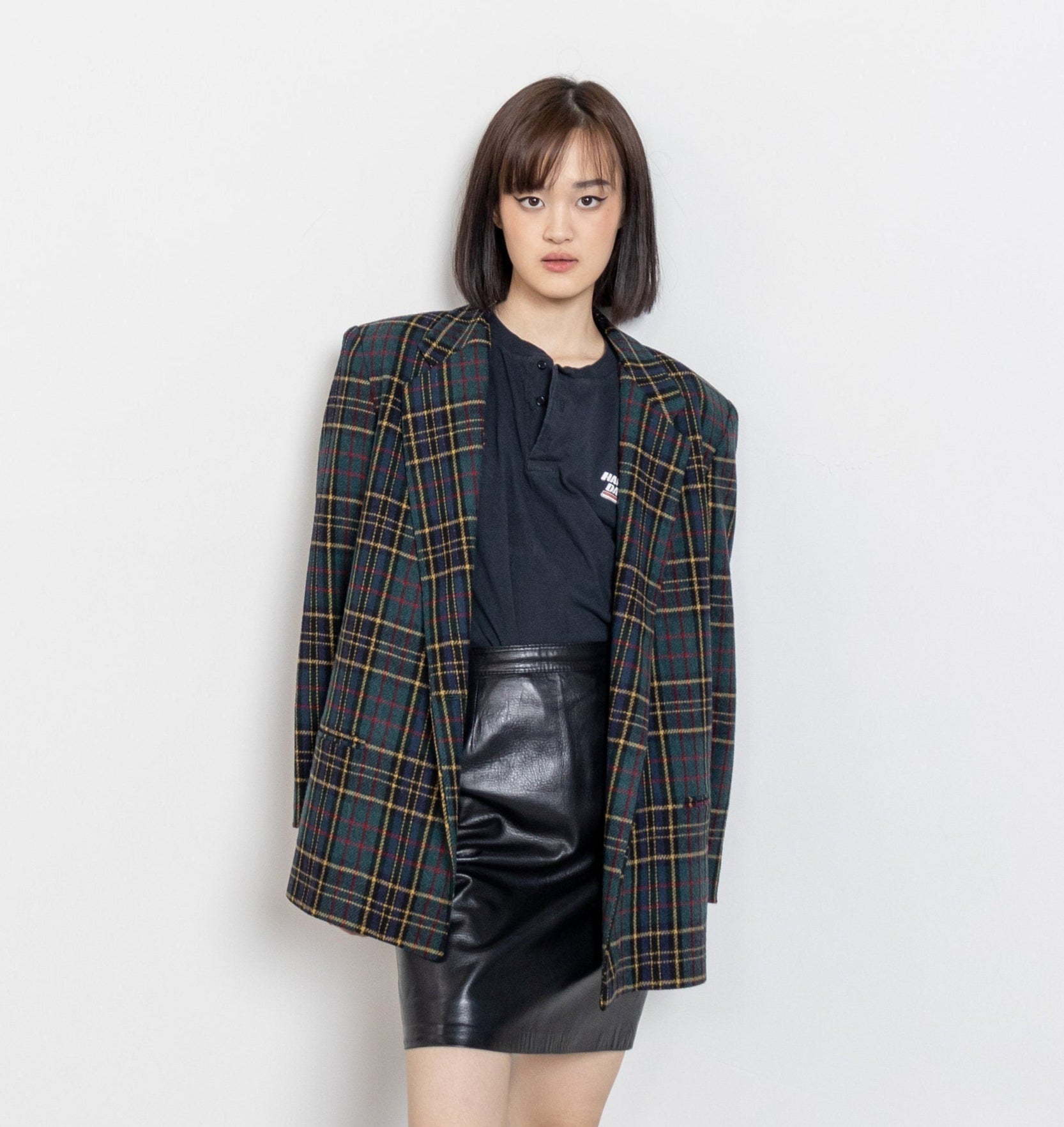 Person wearing a plaid blazer, black leather skirt, and black boots against a white background