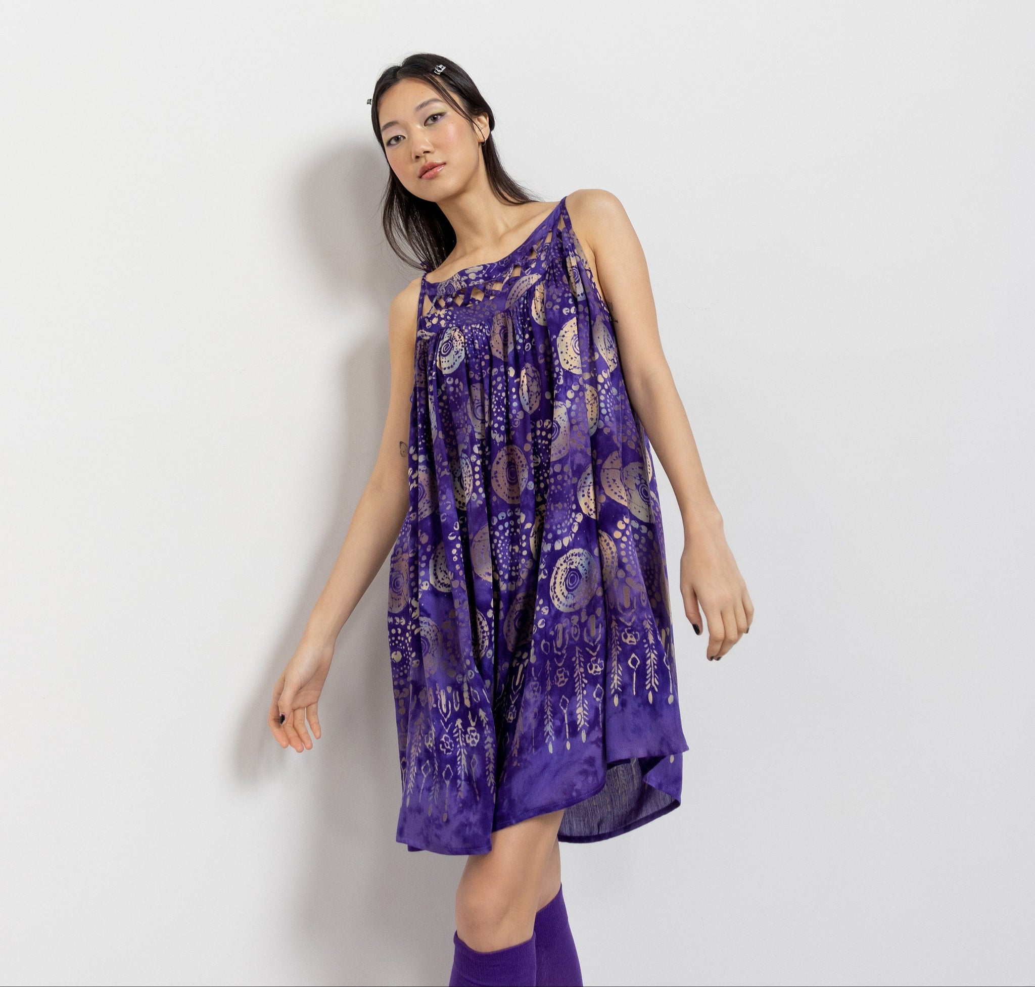 A woman modeling a vintage 90's purple oversize spaghetti strap sun dress with a abstract circular print and woven open detailing at the bodice.