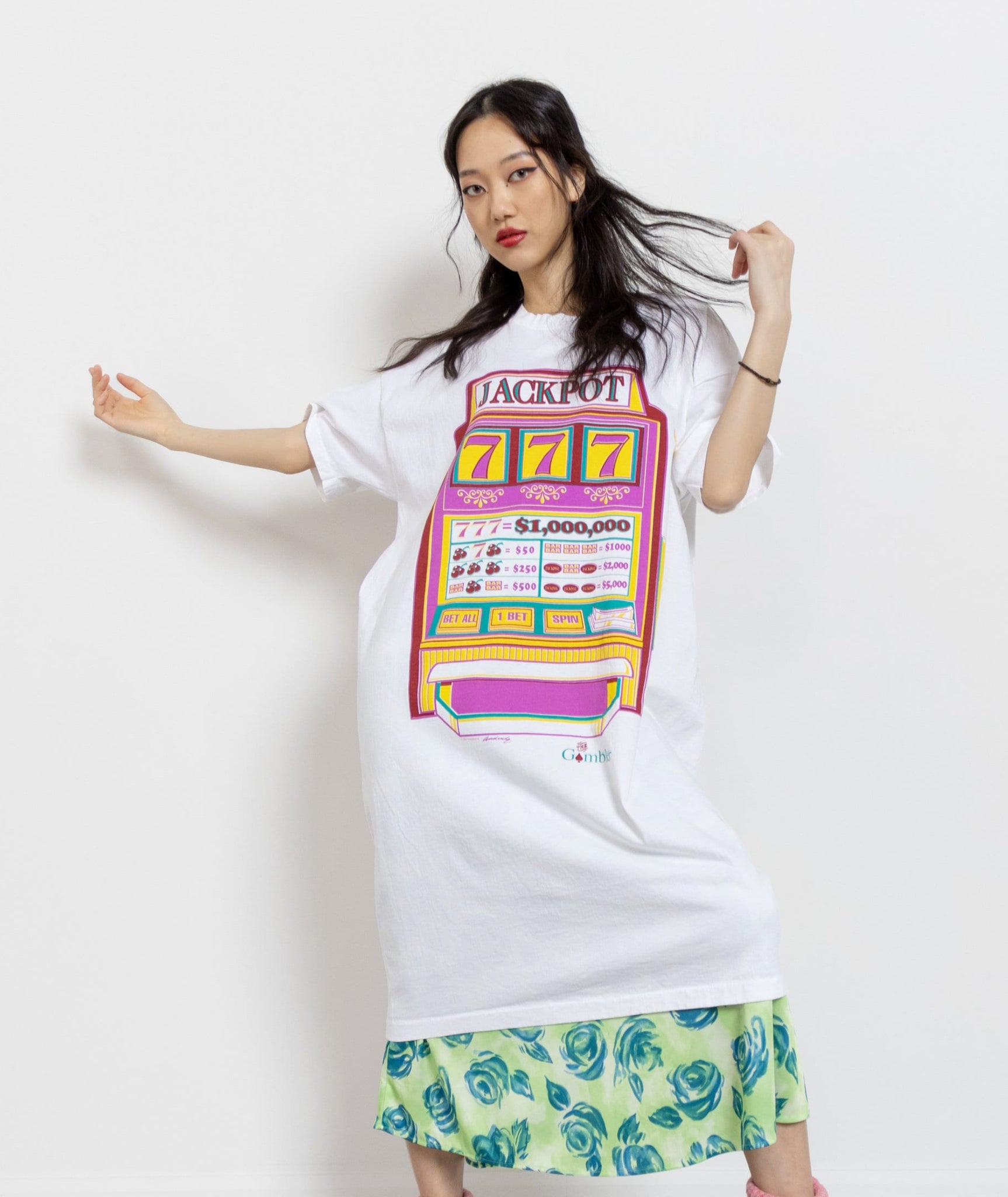 A person wearing a white oversized t-shirt dress with a colorful slot machine print on the front, paired with a patterned skirt.