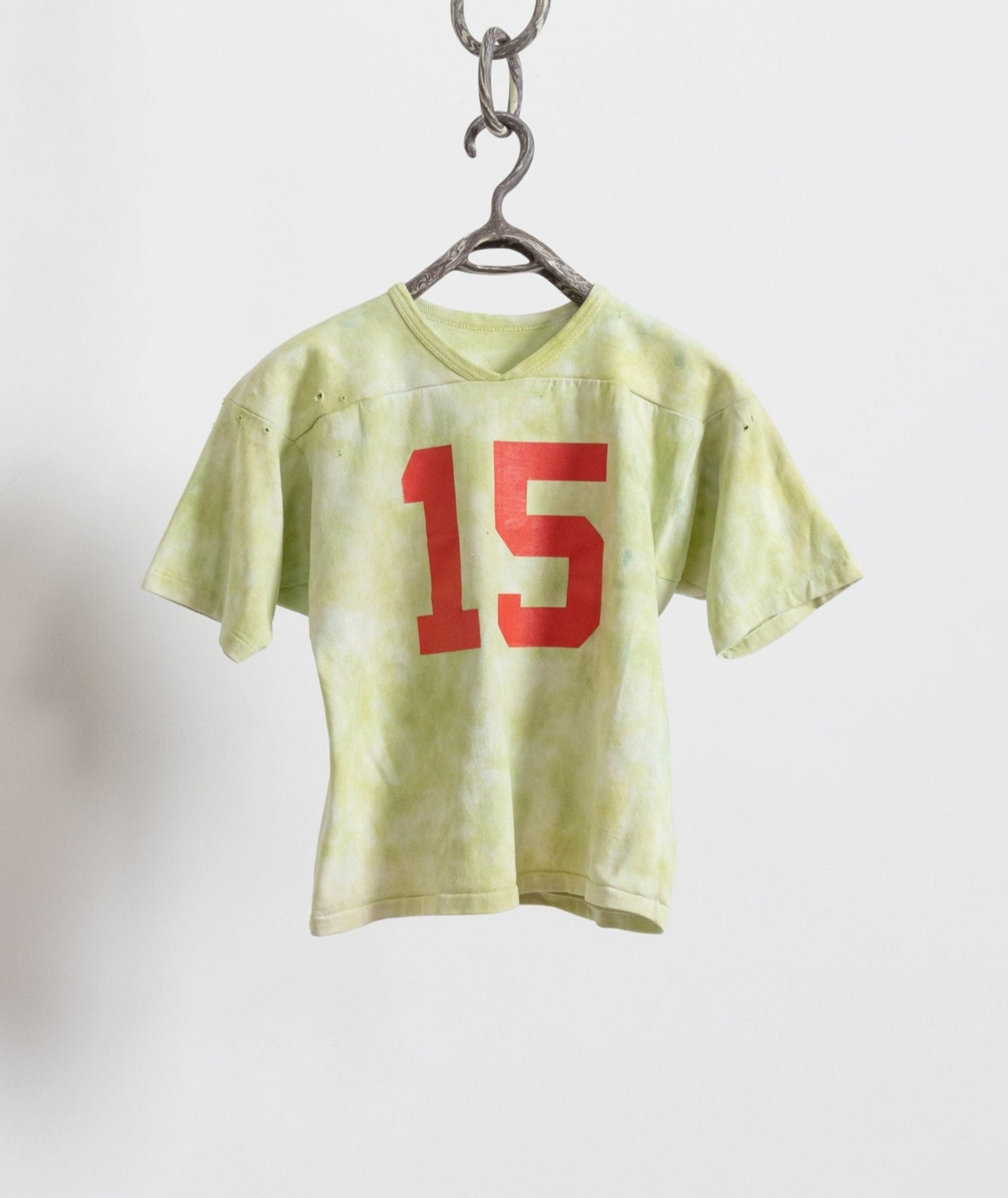 A green tie-dye jersey with the number 15 printed on the front, hanging against a white background.