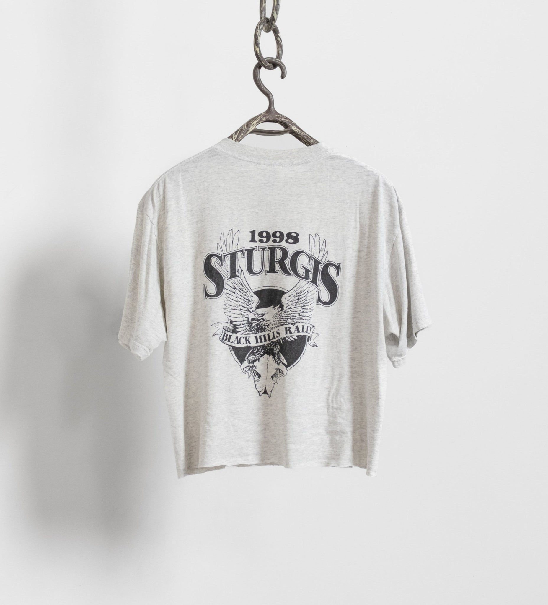 Gray t-shirt with 'Sturgis' graphic design on a hanger against a white background