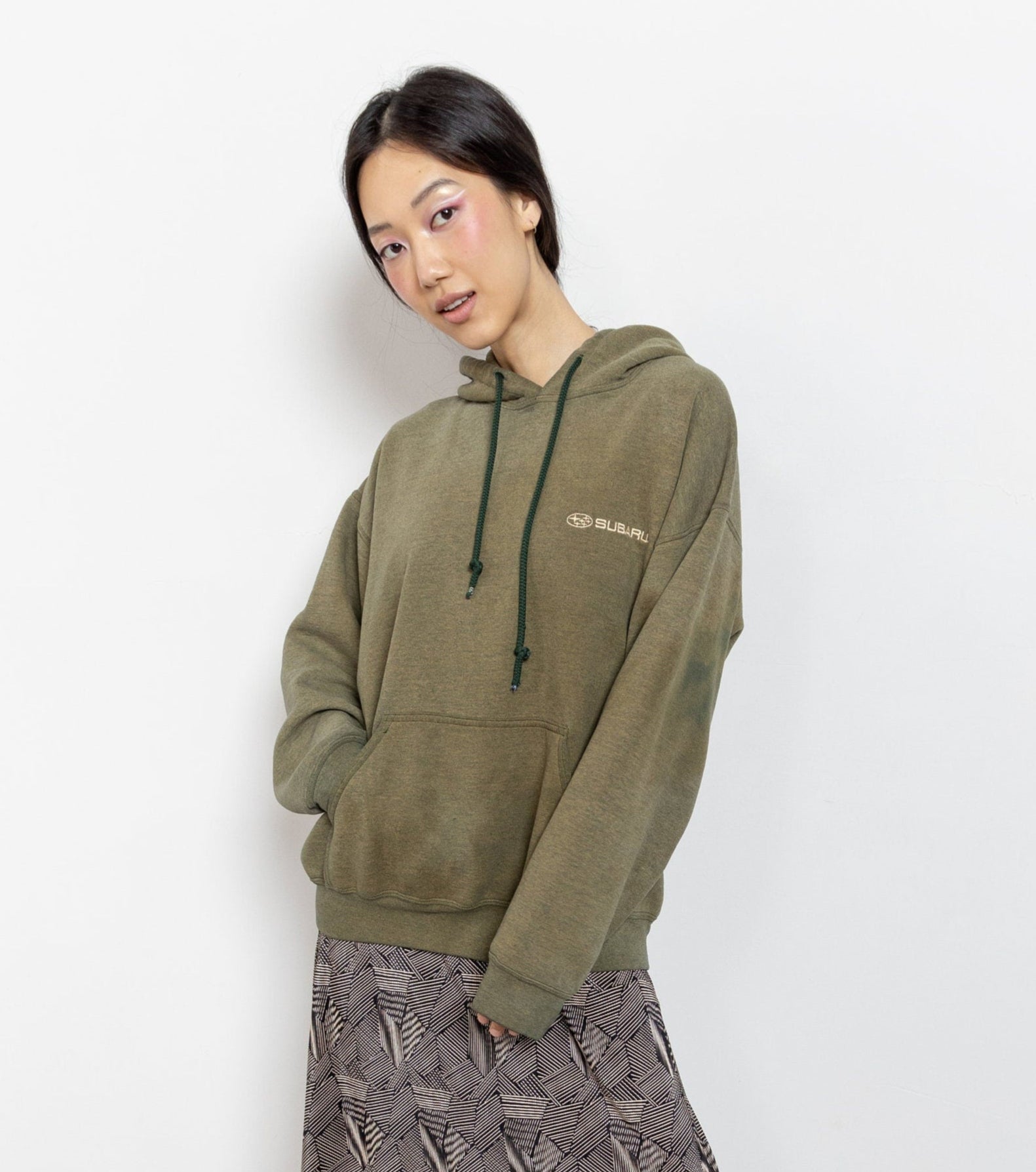Person wearing an olive green hoodie with a brand logo on a white background