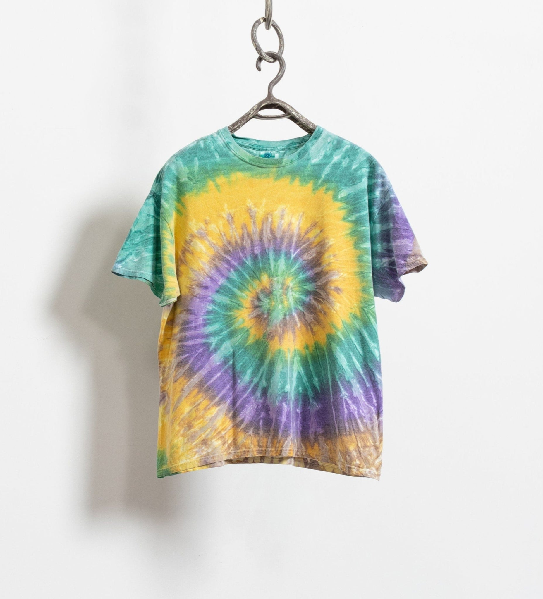 A vintage 90's bright rainbow tie-dye t-shirt with a spiral pattern in yellow, green, and purple, displayed on a hanger against a white background.