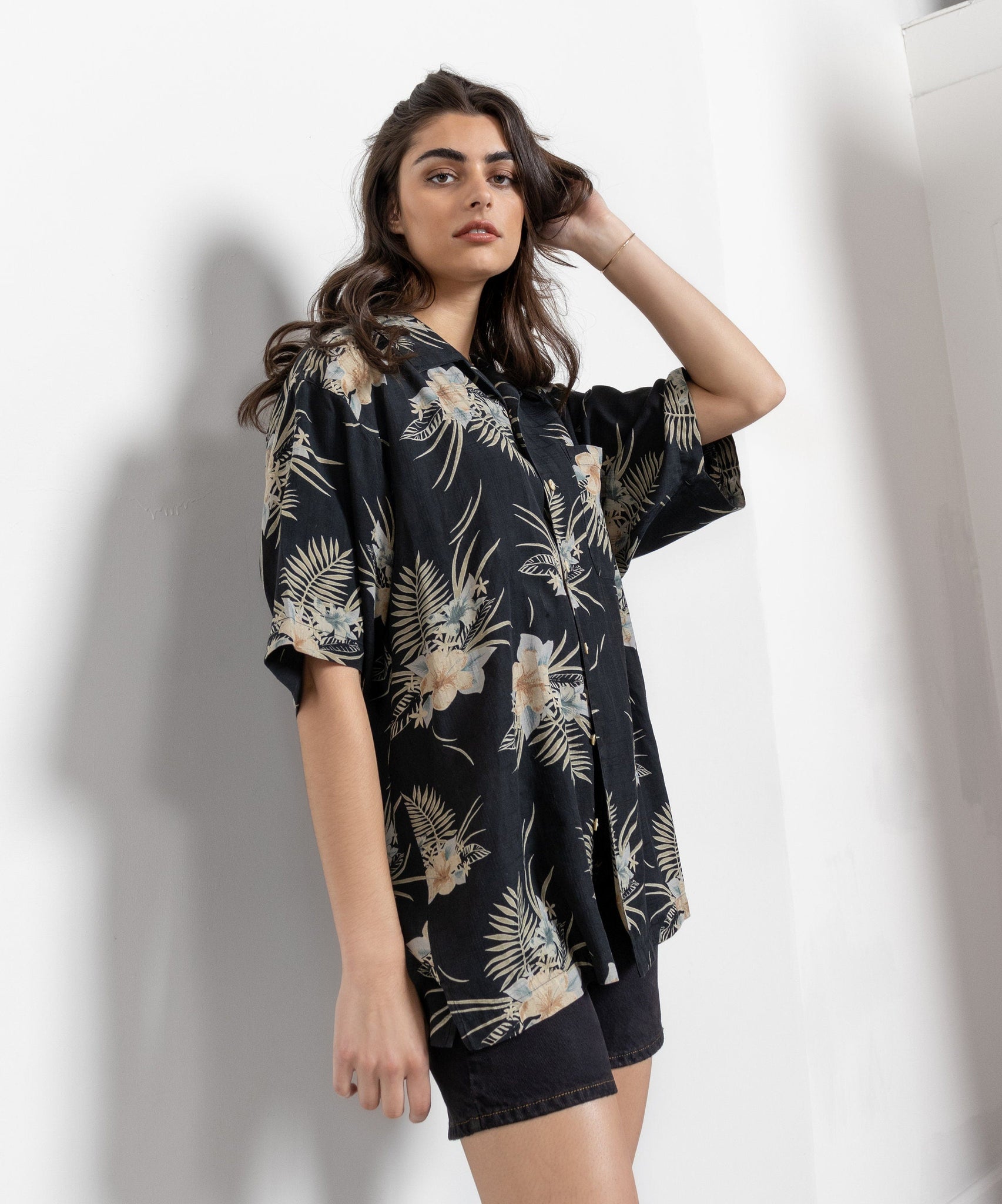 A woman modeling a black tropical floral blouse with short sleeves and shorts.