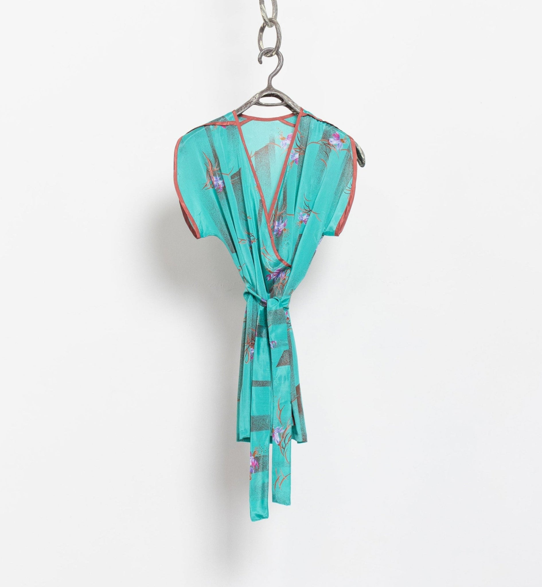 Vintage 90's teal sleeveless mini wrap dress with a floral pattern, tied at the waist, hanging on a hanger against a white background.