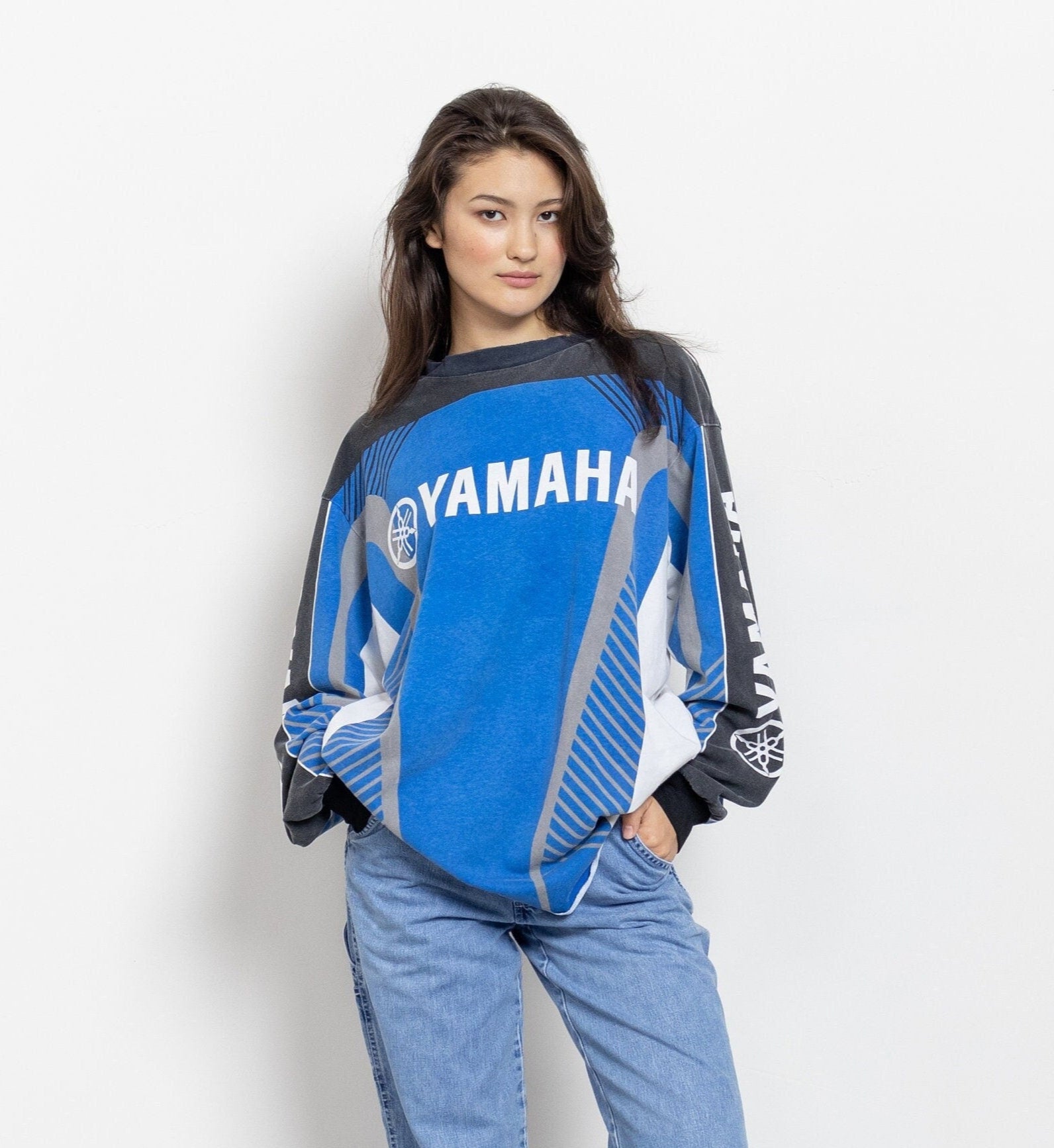 A person wearing a long sleeve vintage Yamaha t-shirt in blue and black with the brand name and logo printed on it.