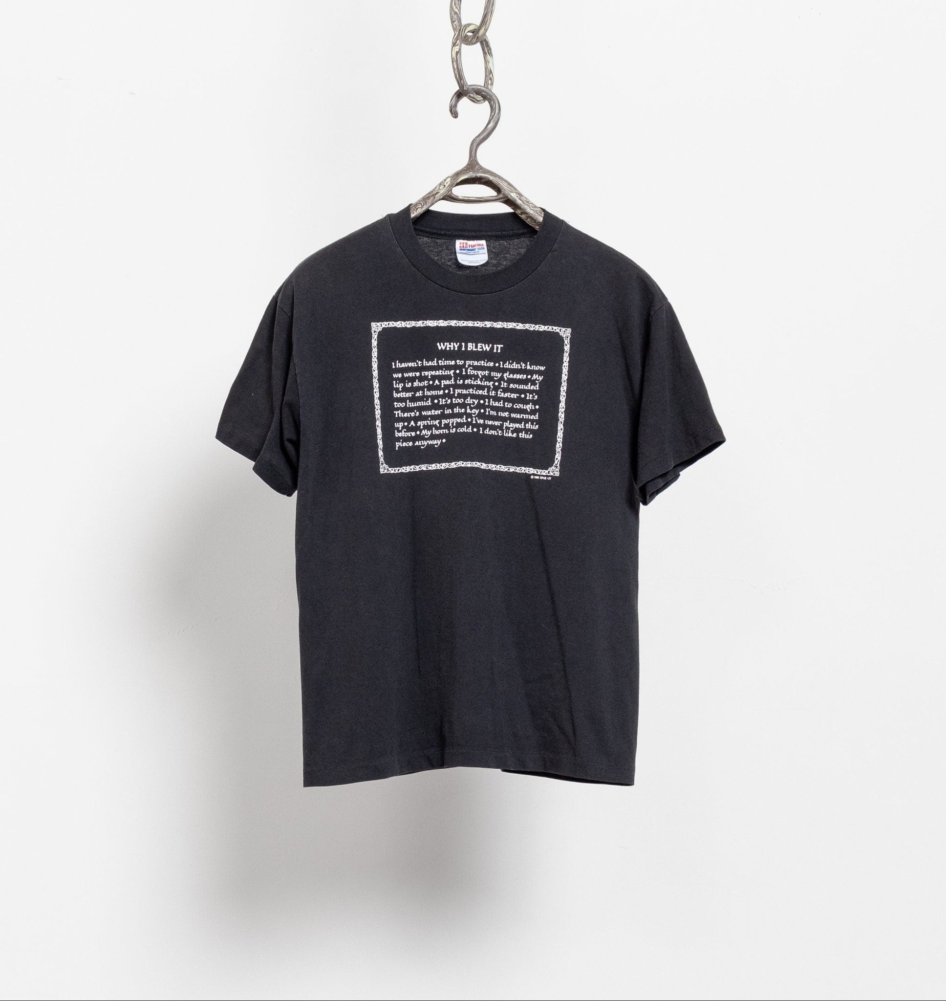 A black vintage humor t-shirt with white text printed on the front, hanging on a hanger against a white background.