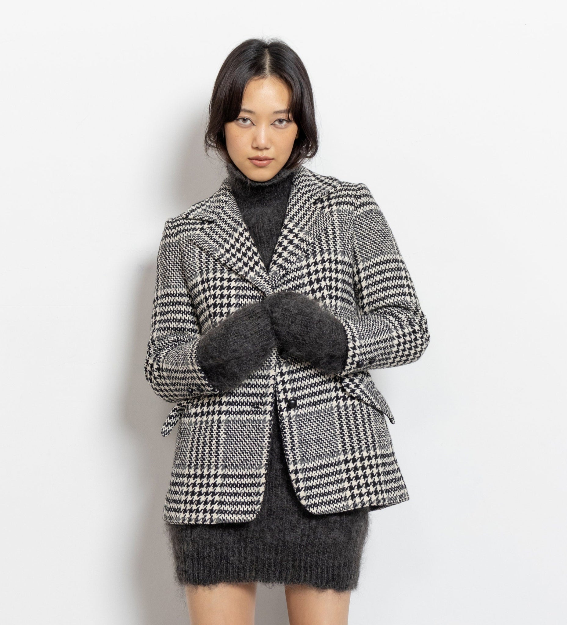 Person wearing a checkered blazer, black sweater, skirt, and knee-high boots on a white background