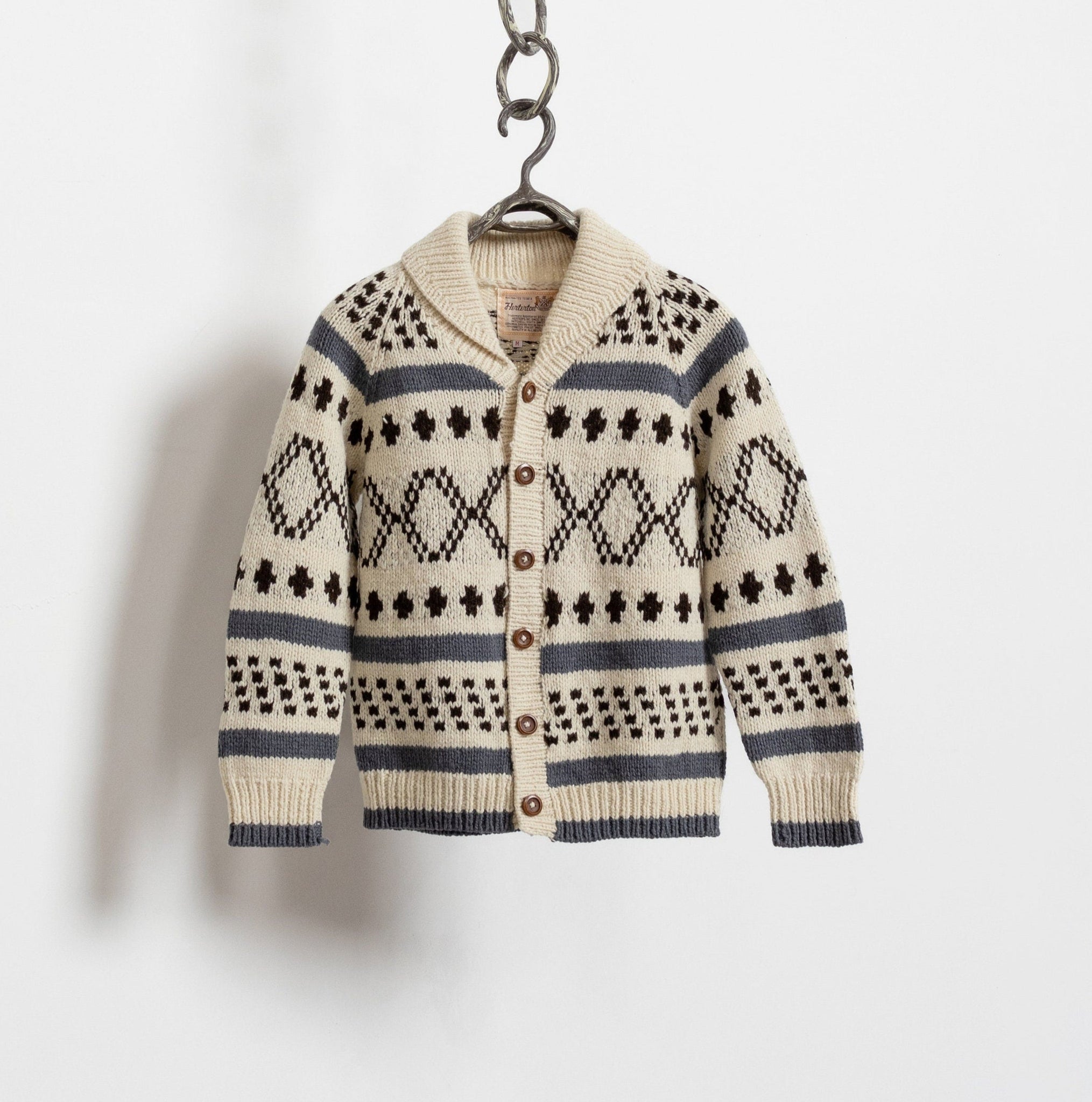 A vintage 90's hand-knit cardigan with a relaxed fit, featuring buttons down the front and oversized wooden buttons. The cardigan is primarily beige with blue and dark stripes, and it is displayed against a white wall.