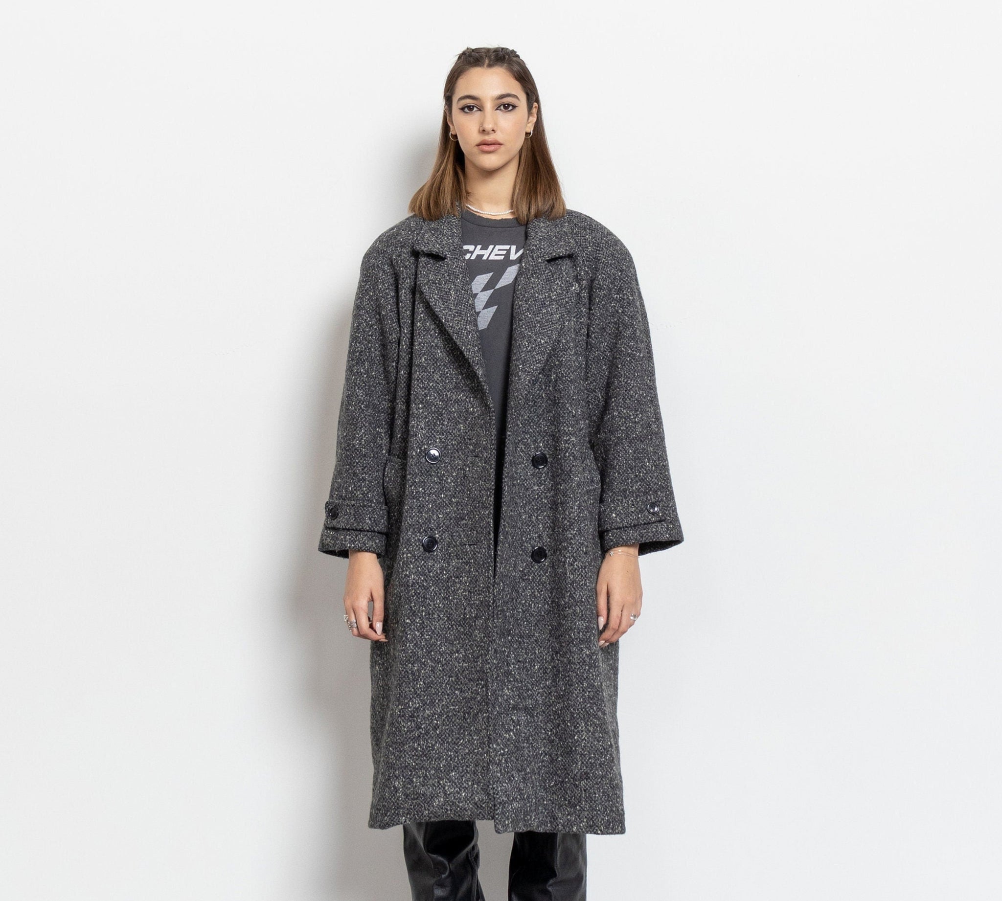 Woman wearing a long gray coat over a graphic t-shirt on a white background