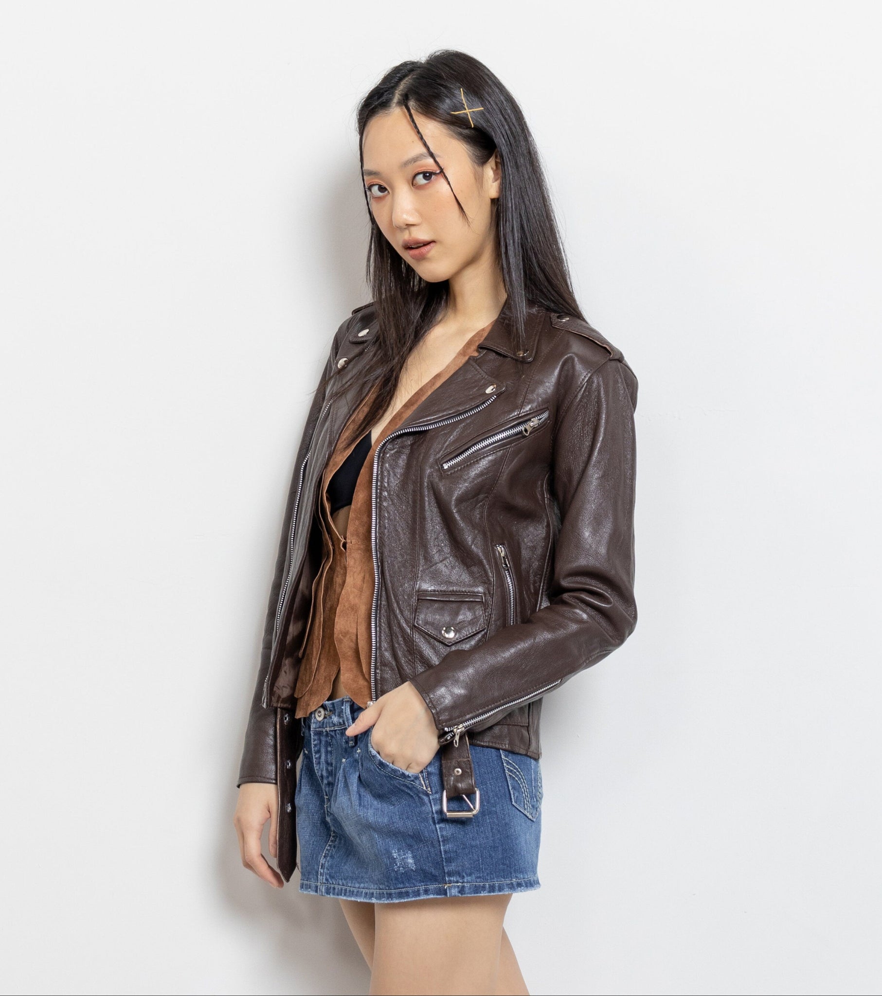 Woman wearing a brown leather jacket and denim skirt on a white background