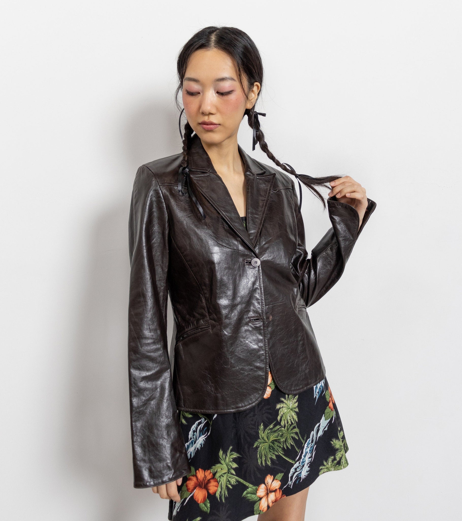Woman wearing a shiny black jacket and a floral dress on a white background