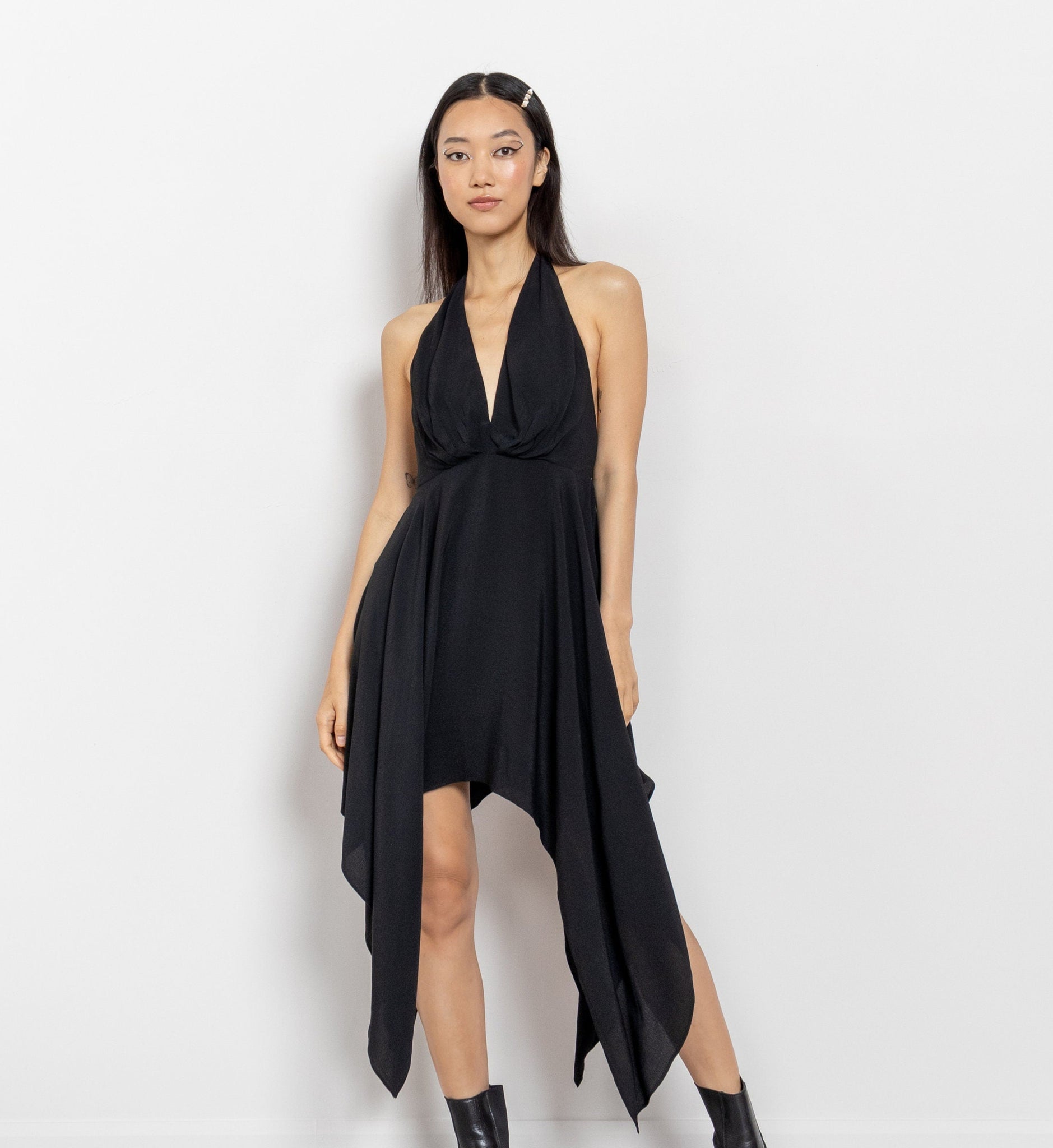 A woman modeling a vintage black halter neck midi dress with a hanky hem, standing against a white background.